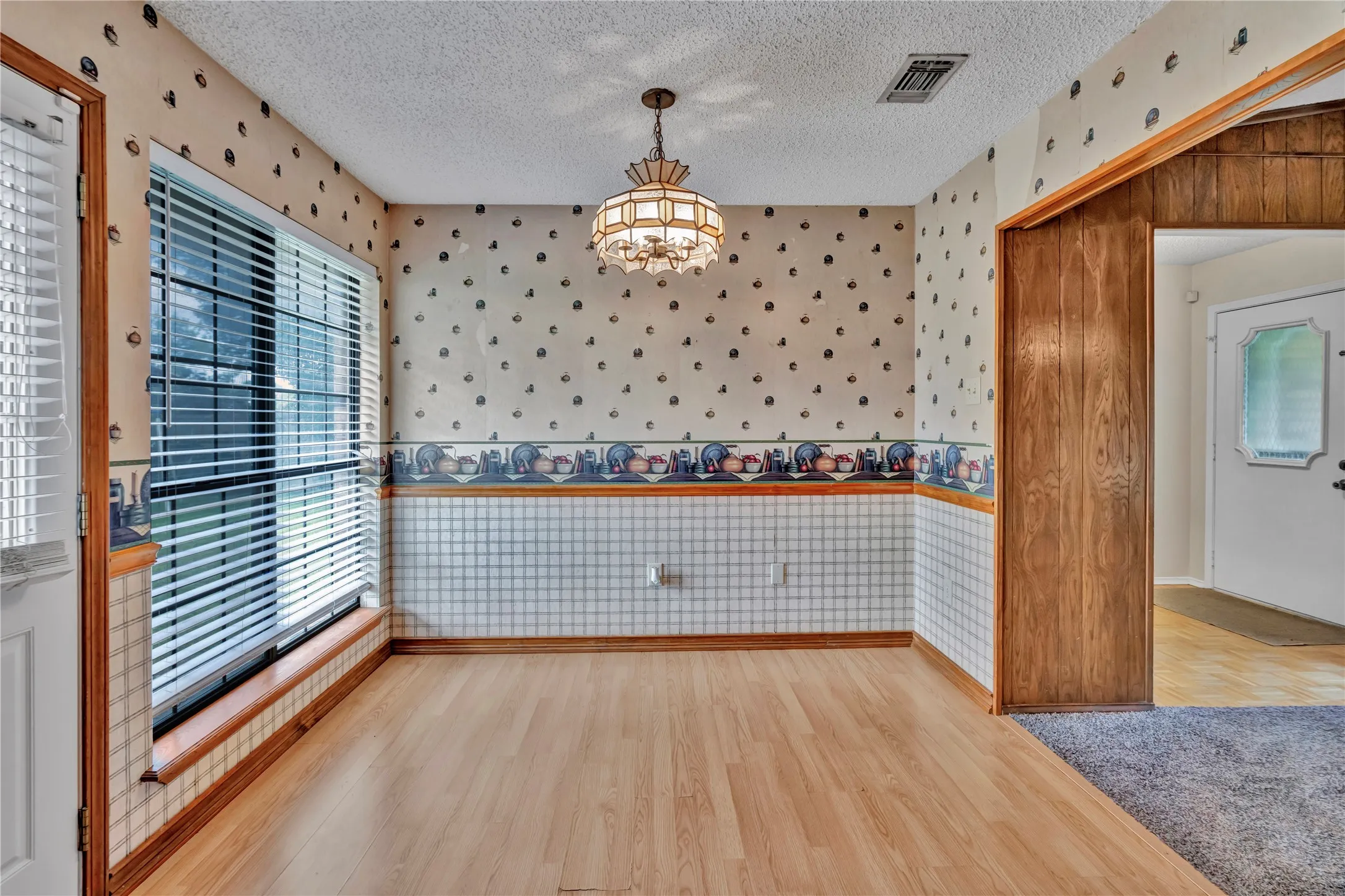 Spacious room featuring wood-finish flooring, a large window with blinds, and a decorative ceiling light fixture