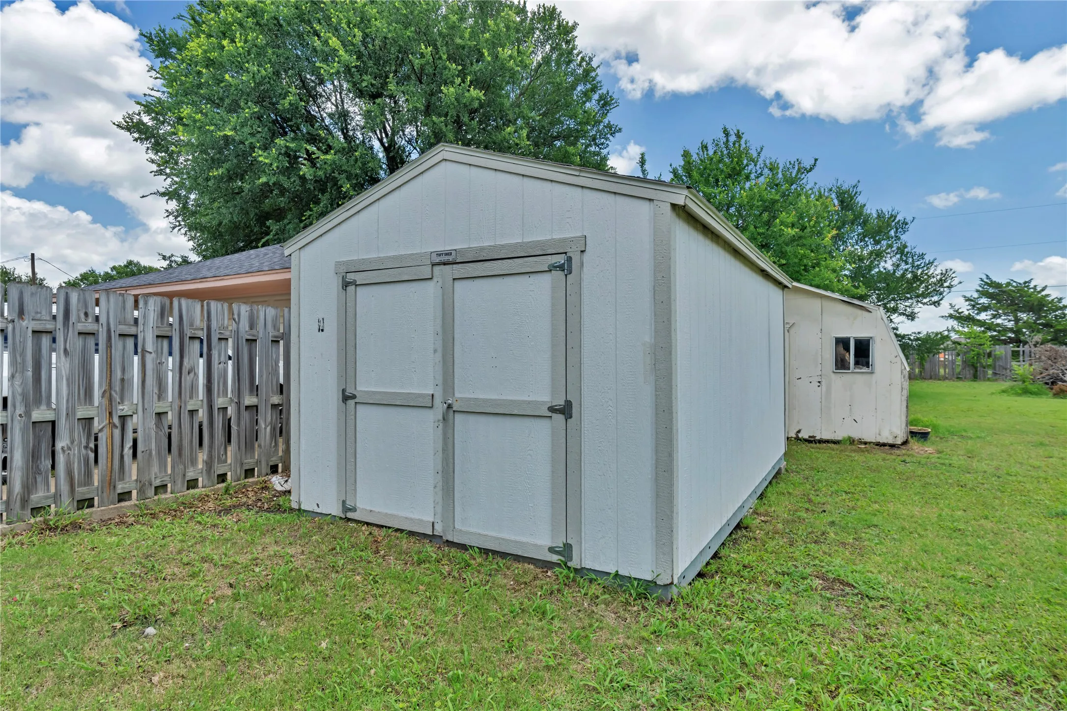 White storage shed with double doors, wood fencing, and a grassy perimeter