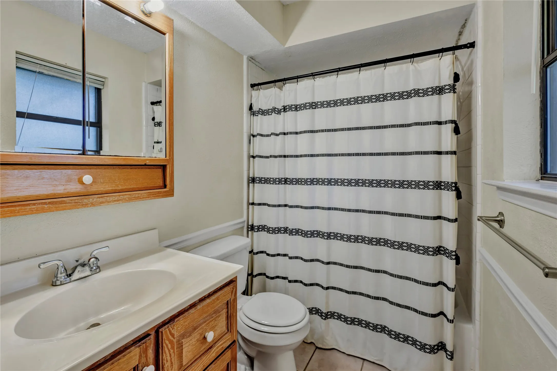 Bathroom featuring a wood-finish vanity with a white countertop and integrated sink, a mirrored medicine cabinet, and a shower/tub combination with white tile surround
