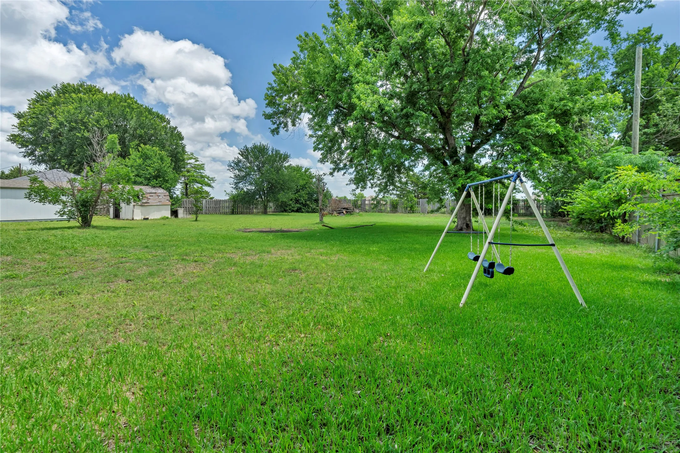 Expansive green lawn with mature trees and a swing set