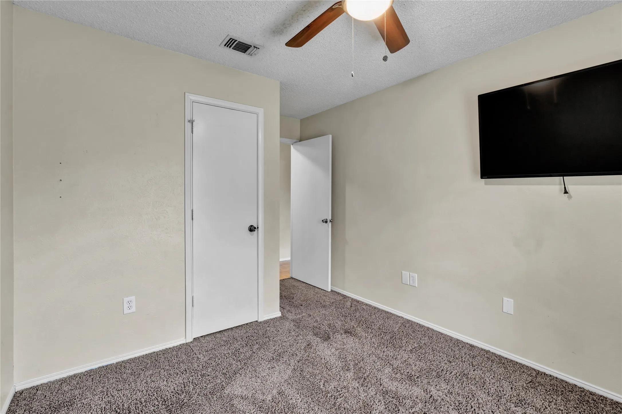 Carpeted room featuring a ceiling fan with integrated lighting, a wall-mounted television, and neutral-toned walls