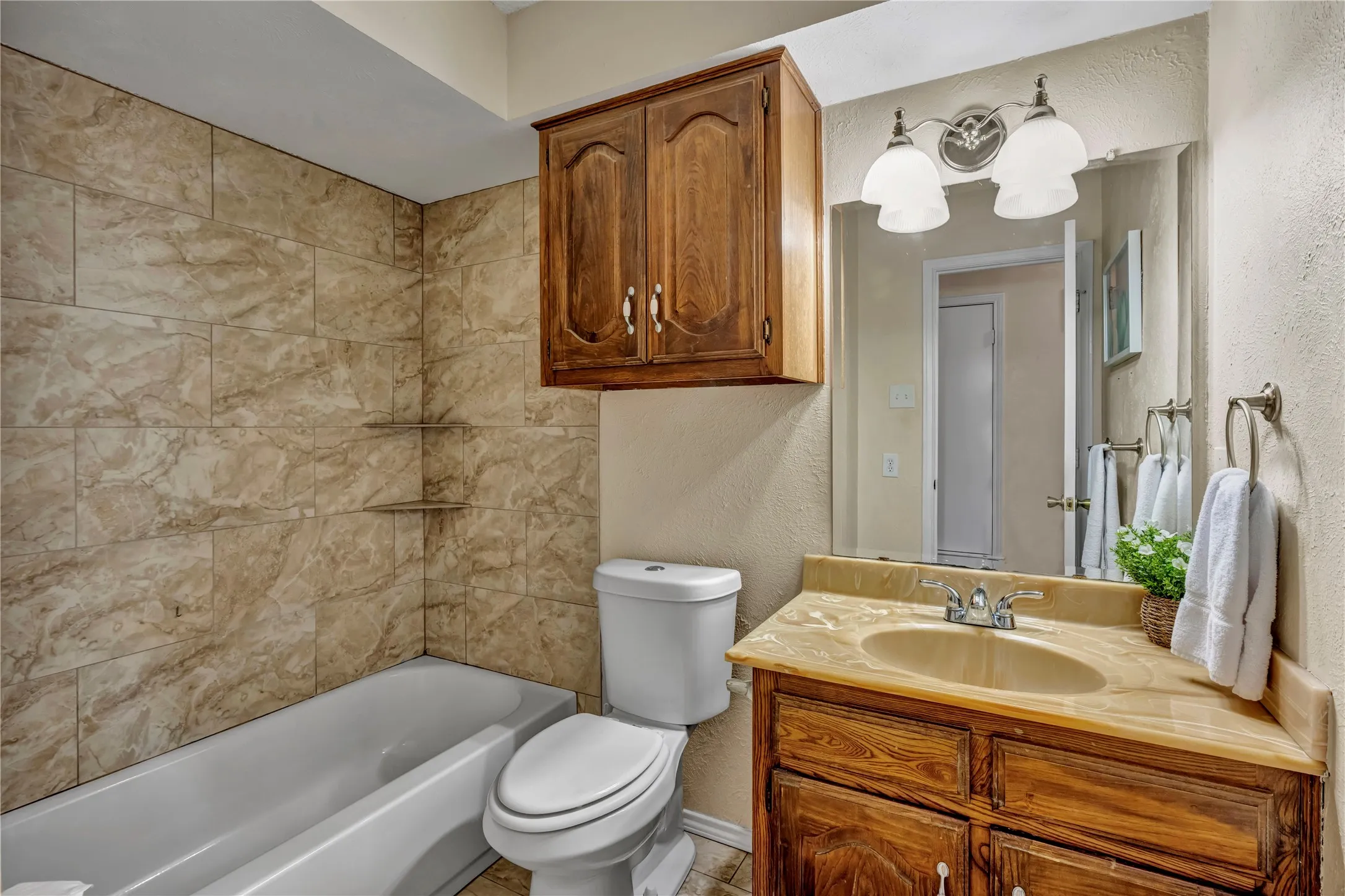 Bathroom featuring a full tub with tiled surround, a corner vanity with an integrated sink, and an overhead wooden storage cabinet