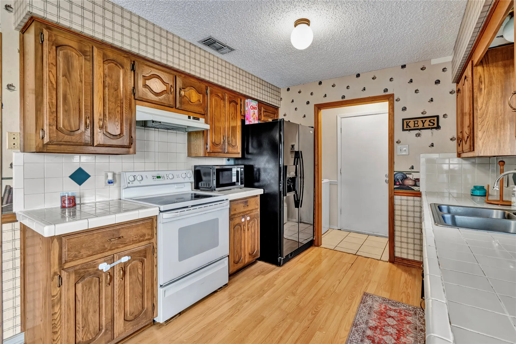 Kitchen featuring wood-finish cabinetry, white tile countertops, and light wood-finish flooring