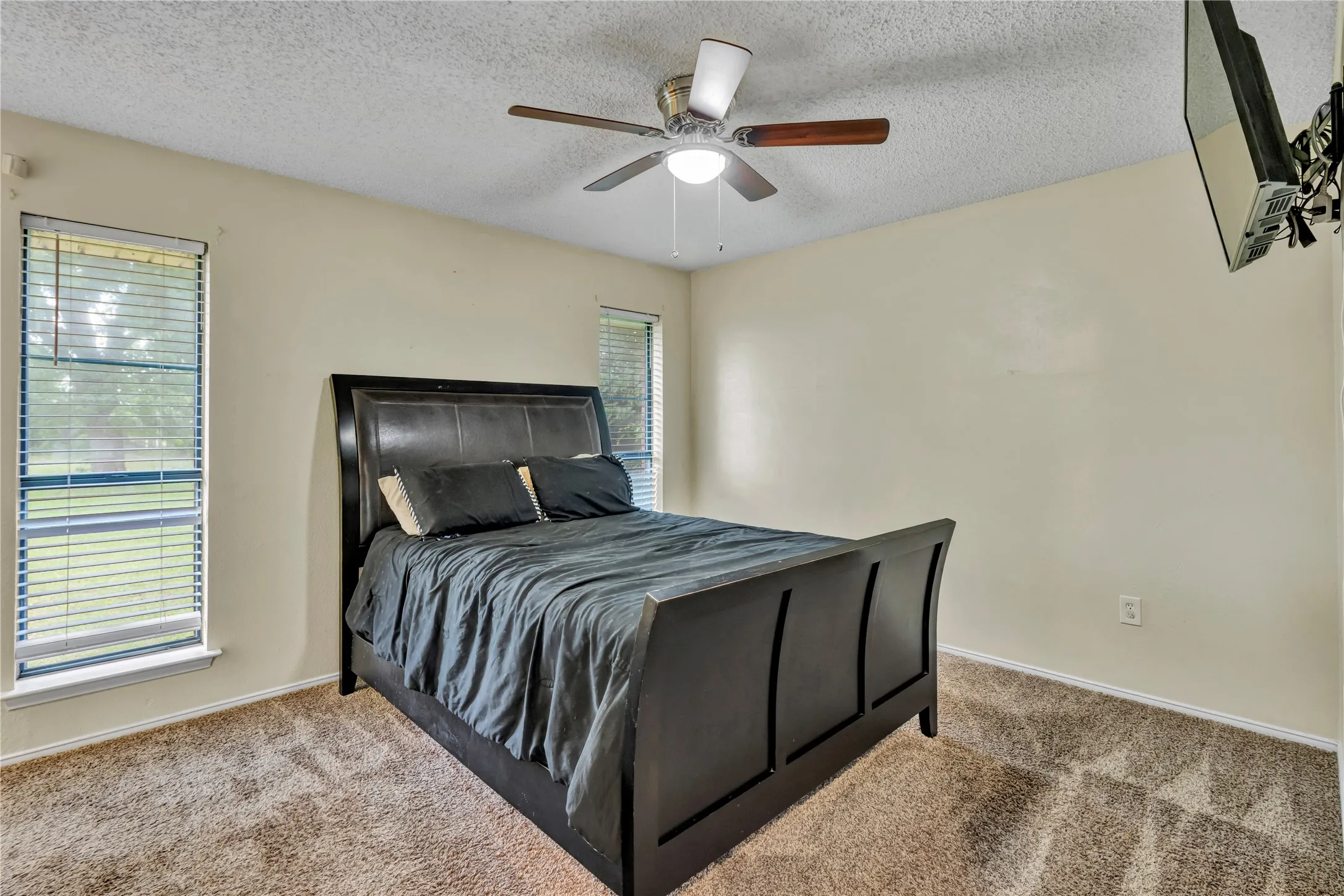 Carpeted room featuring a ceiling fan with integrated lighting, two windows with horizontal blinds, and neutral wall tones