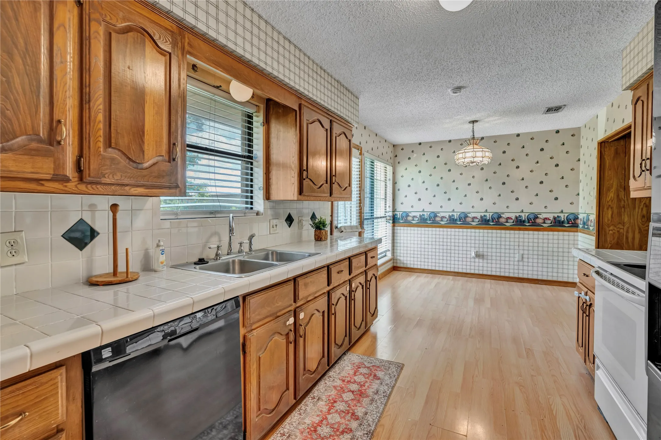 Kitchen area featuring wood-finish cabinetry, a dual basin stainless steel sink, and white tile countertops with a coordinating backsplash