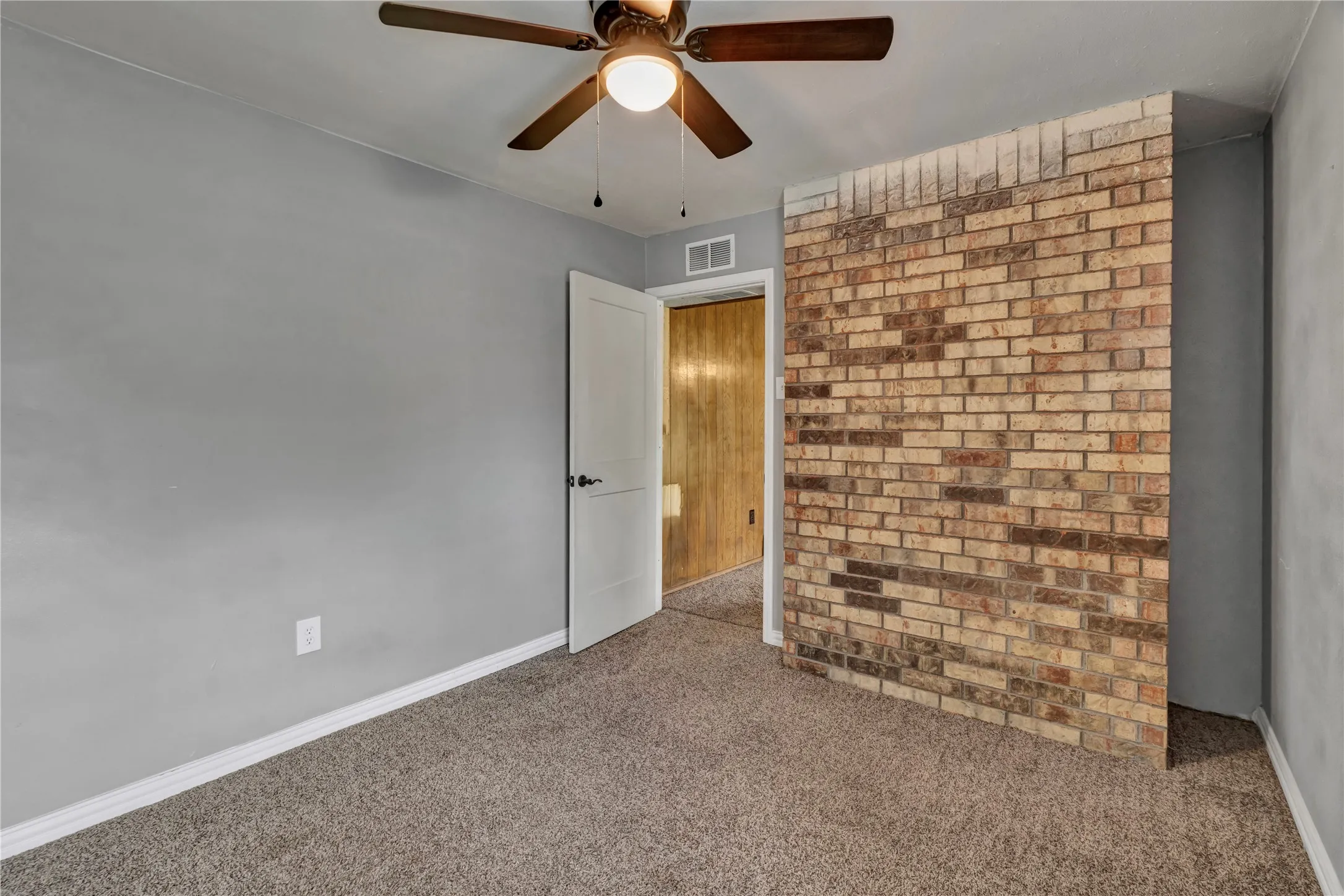 Interior space featuring a partial brick accent wall, neutral carpeting, and light gray painted walls