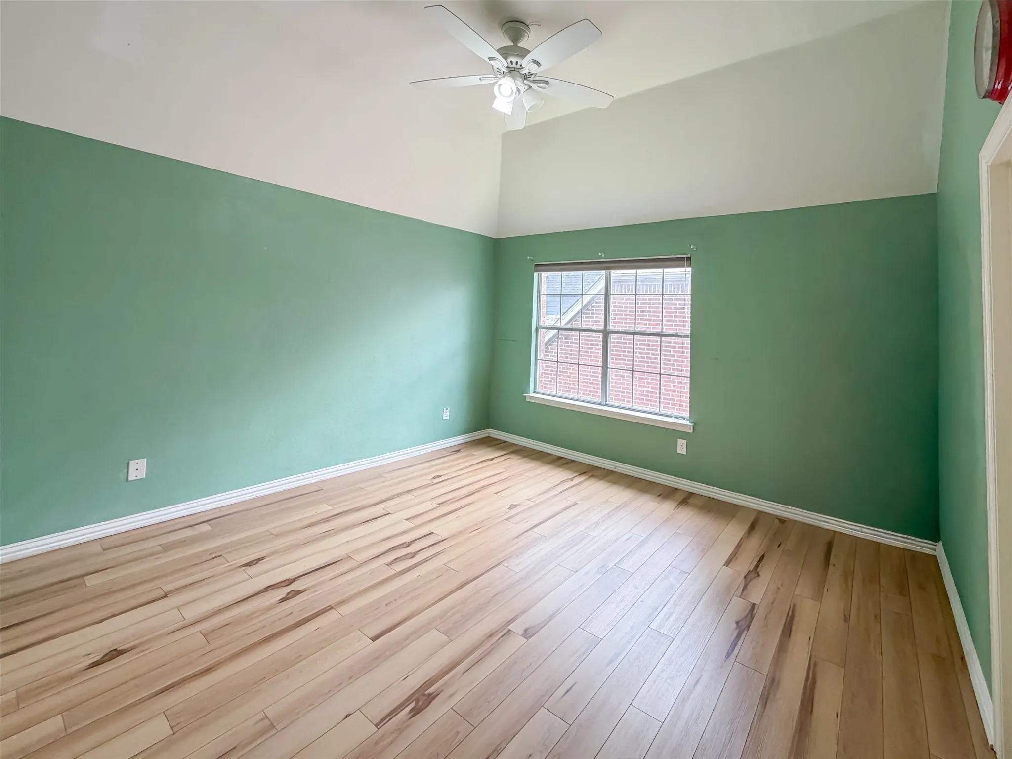 Room featuring vaulted ceilings, wood-finish flooring, a ceiling fan, and a large window with white trim