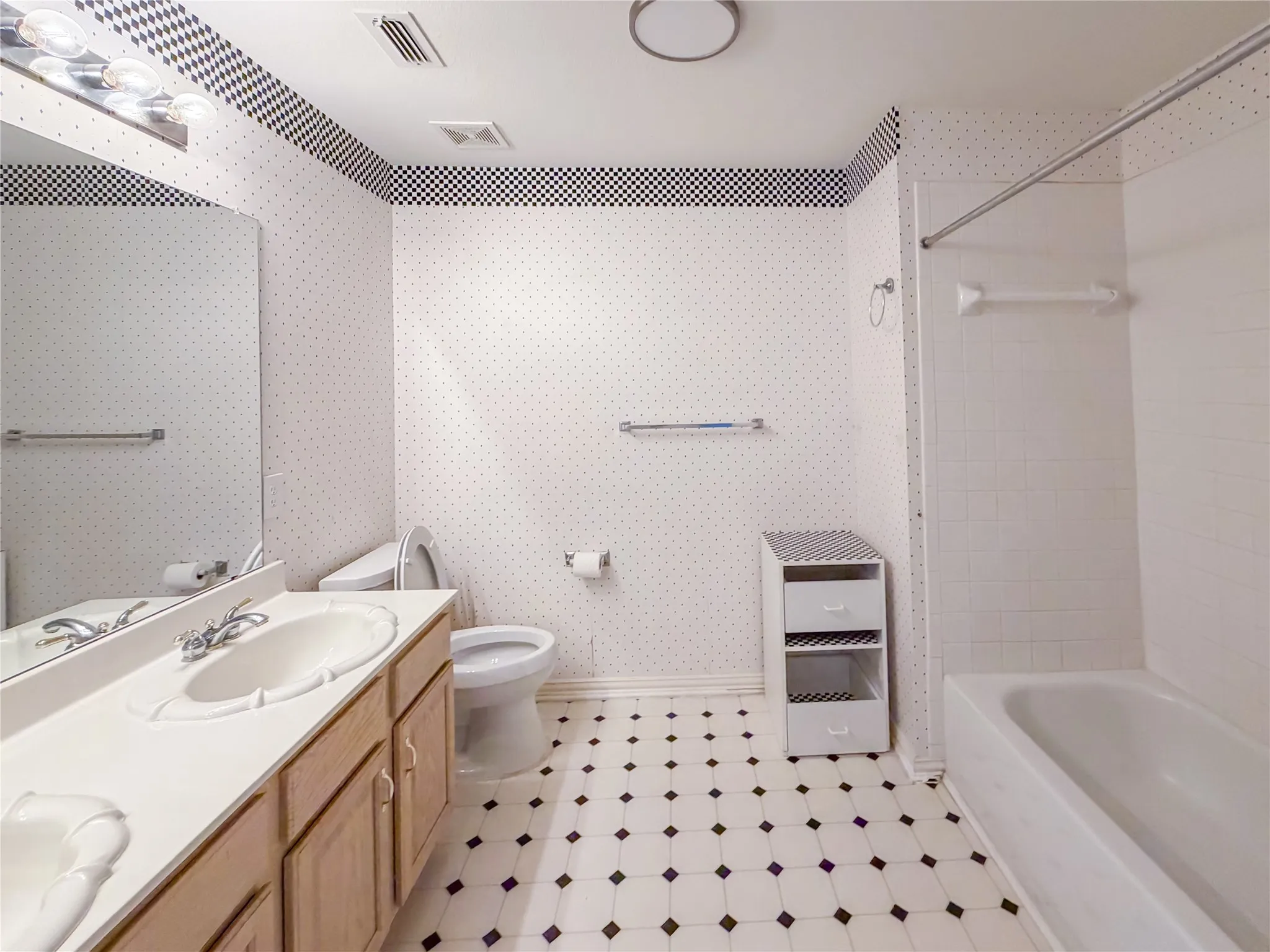 Bathroom featuring a vanity with an integrated sink, a large wall mirror, a bathtub with a shower, a toilet, and patterned floor tiling