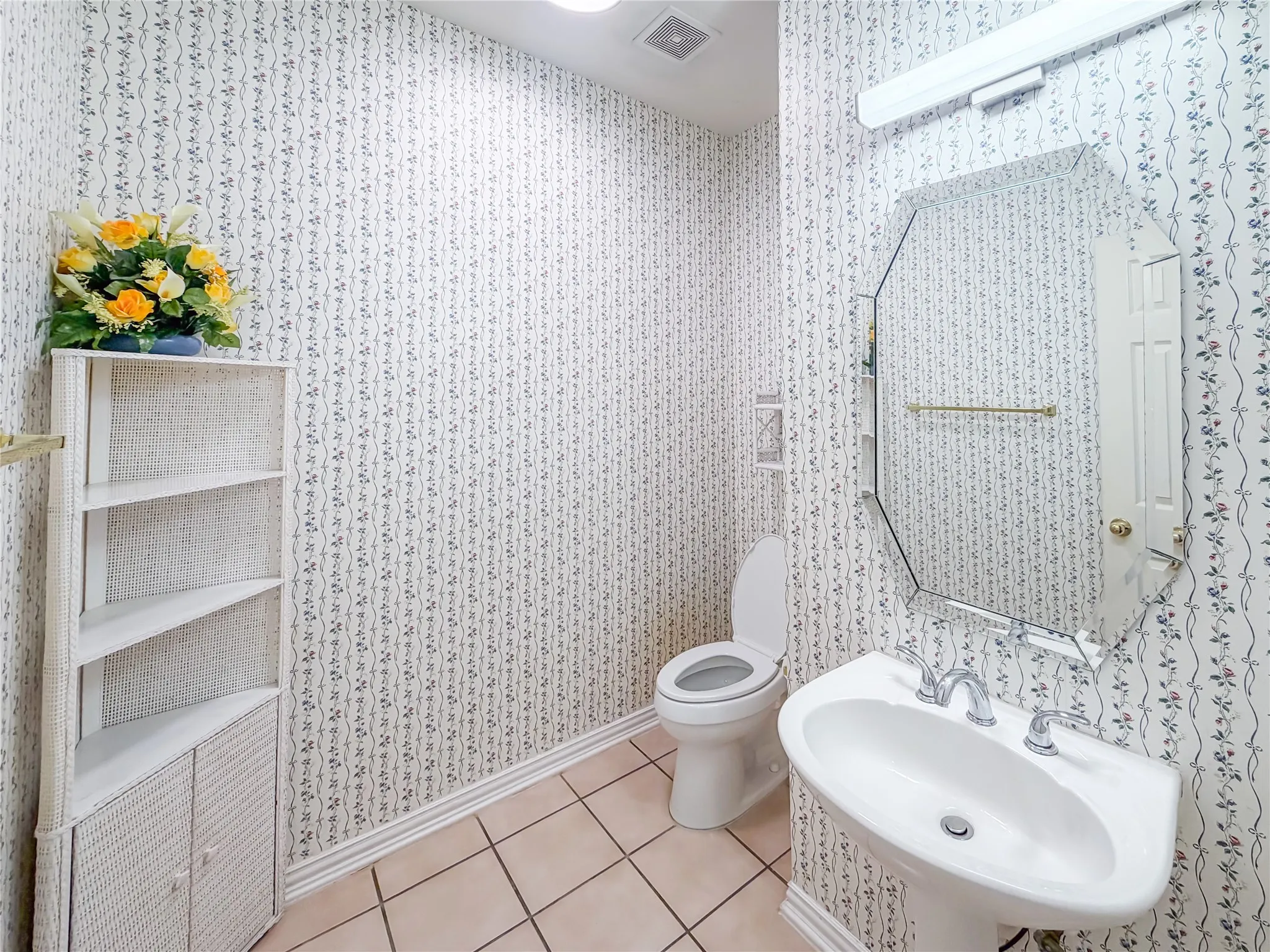 Pedestal sink with chrome faucet, octagonal wall mirror, and patterned wallpaper