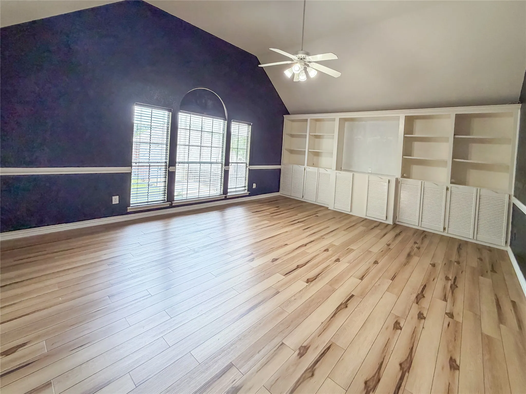 Vaulted ceiling living space featuring wood-finish flooring, a ceiling fan, and built-in shelving with cabinet storage