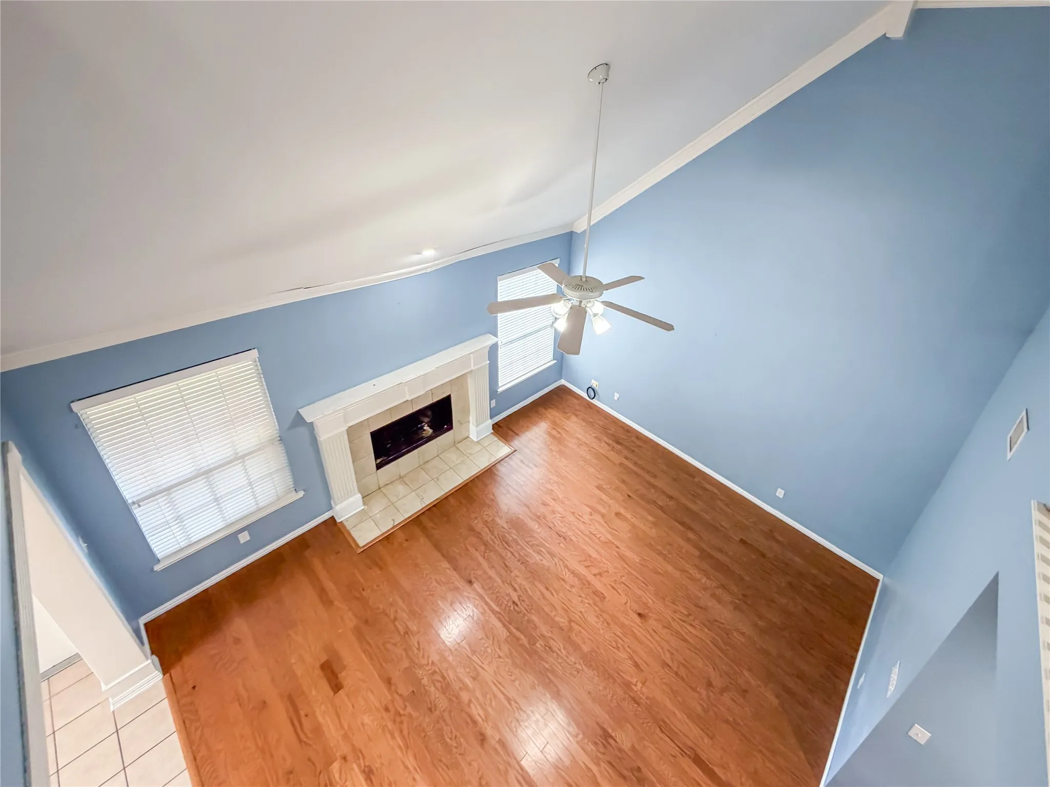 Living area featuring wood-finish flooring, a fireplace with a tiled hearth and mantel, vaulted ceilings, and a ceiling fan with integrated lighting