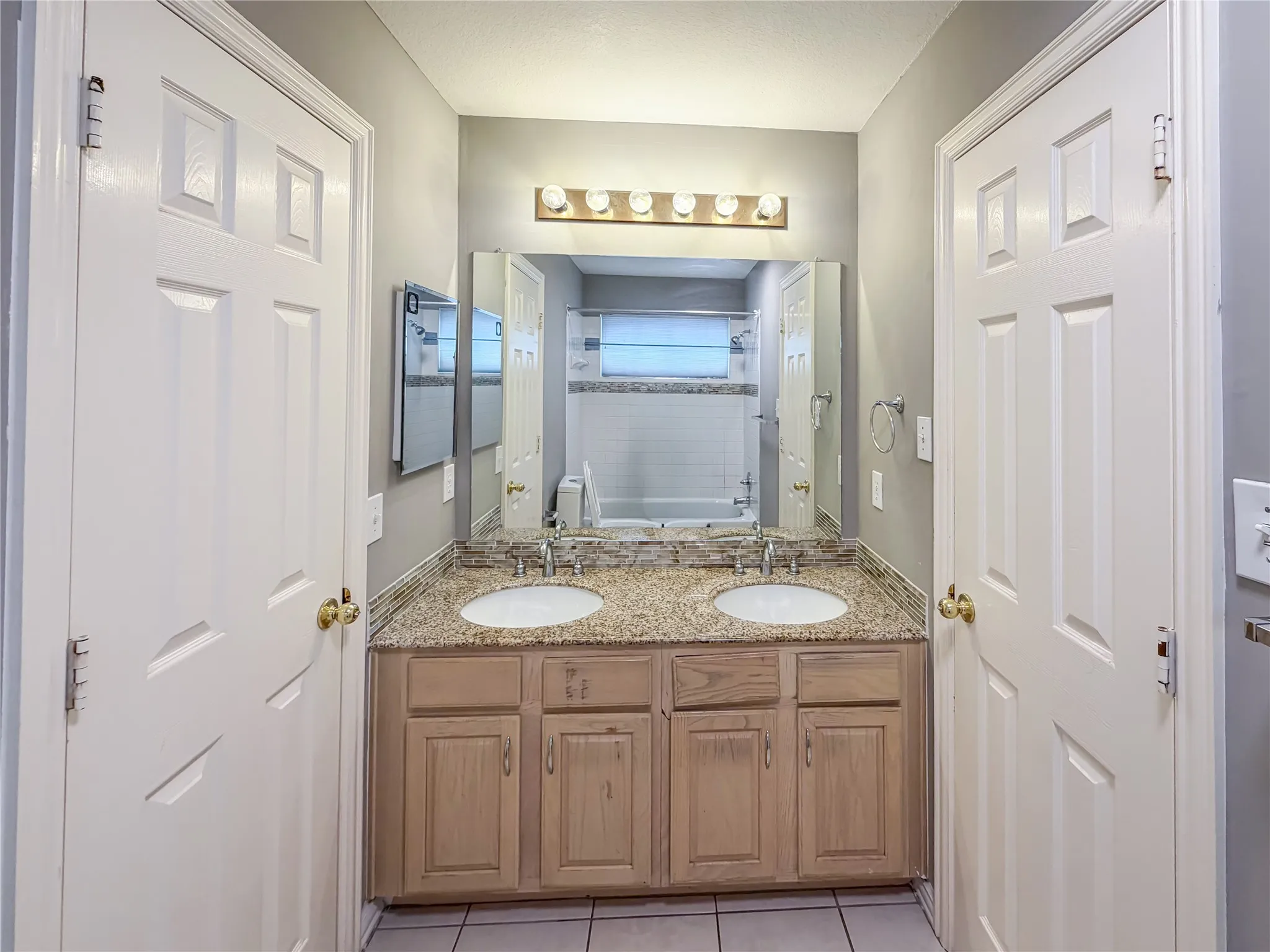 Bathroom featuring a dual vanity with light-toned cabinetry, a speckled countertop, and two integrated sinks