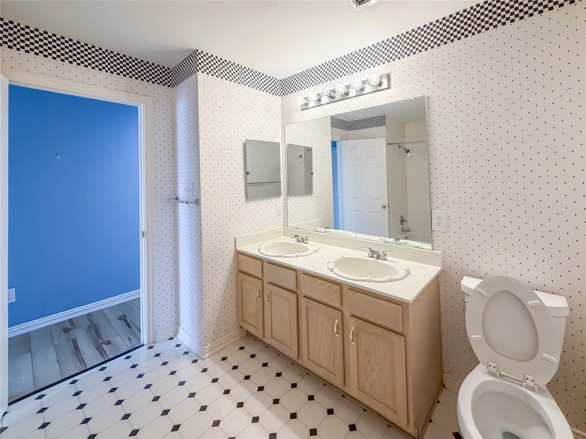 Dual vanity with integrated sinks, light wood-finish cabinetry, and a large wall-mounted mirror