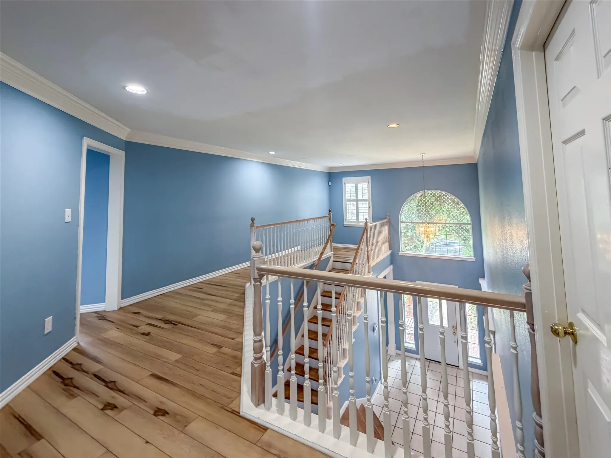 Upper-level landing featuring wood-finish flooring, recessed lighting, and a white baluster railing overlooking the foyer