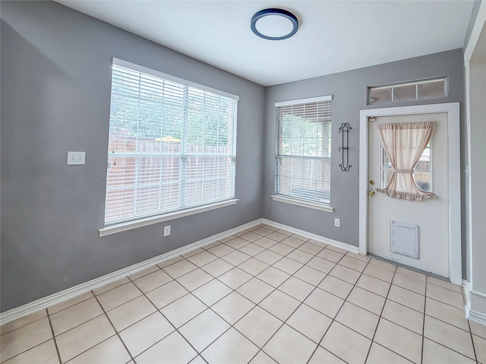 Room featuring diagonal-set tile flooring, two windows with blinds, and a rear door with a transomed window and lower panel