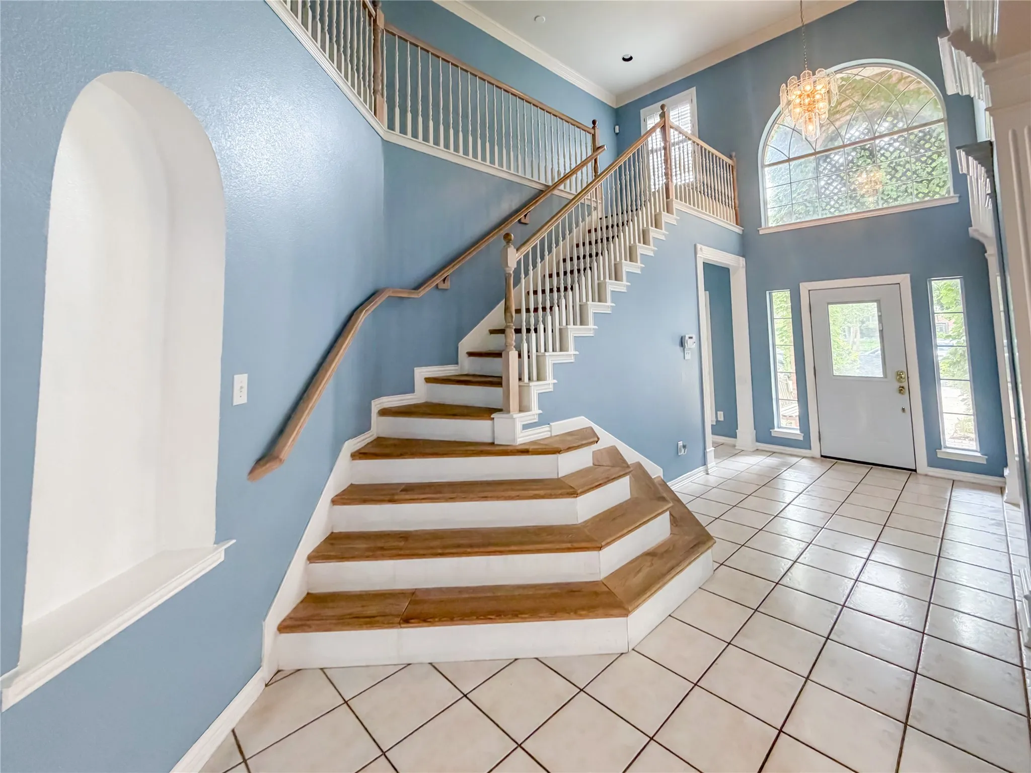 Two-story foyer featuring a grand staircase with wood-finish treads and white risers, a second-story landing with white balusters, an arched window, transom window, and a tile floor