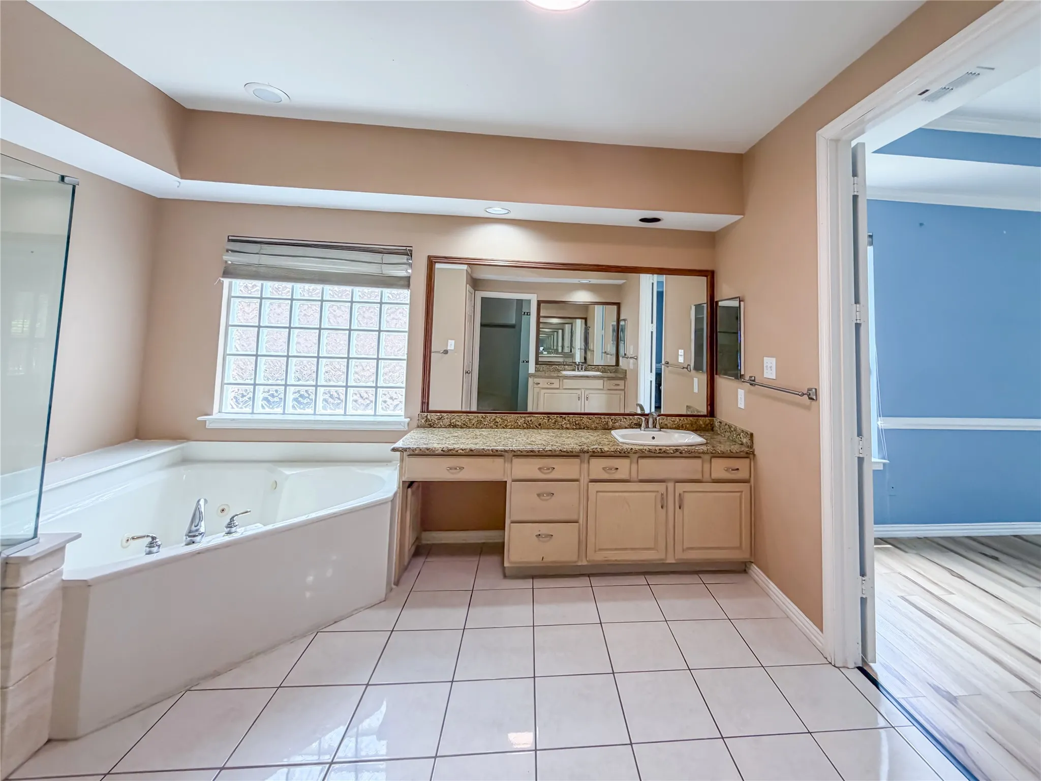Spacious bathroom featuring a corner soaking tub, glass block window, and a vanity with an integrated sink