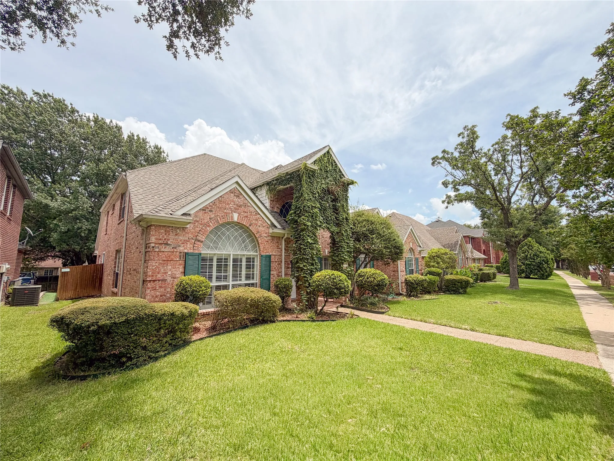 Brick exterior featuring an arched window, decorative shutters, and mature ivy detailing