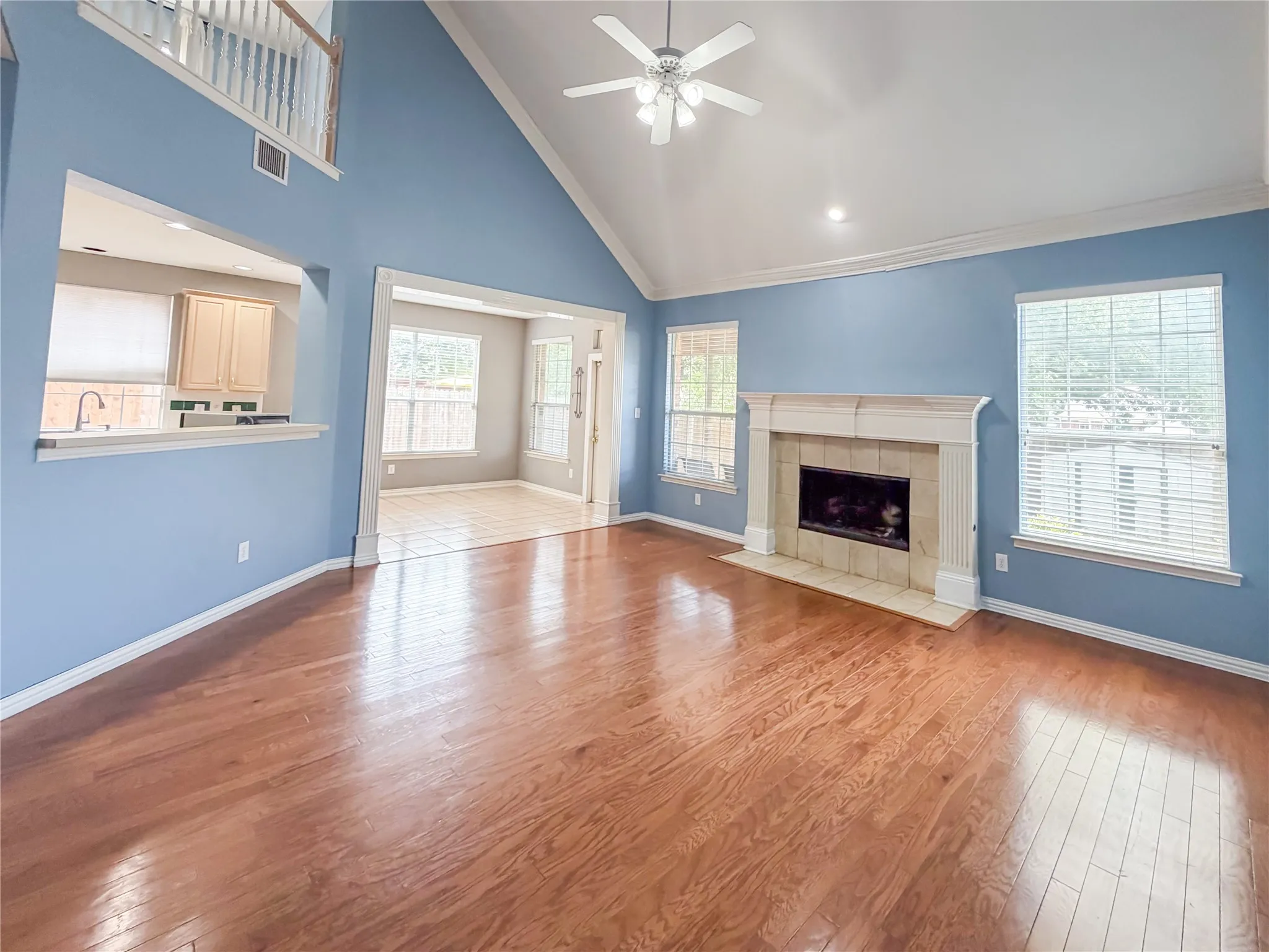 Spacious living area featuring wood-finish flooring, a vaulted ceiling, and a fireplace with a decorative mantel and tiled hearth