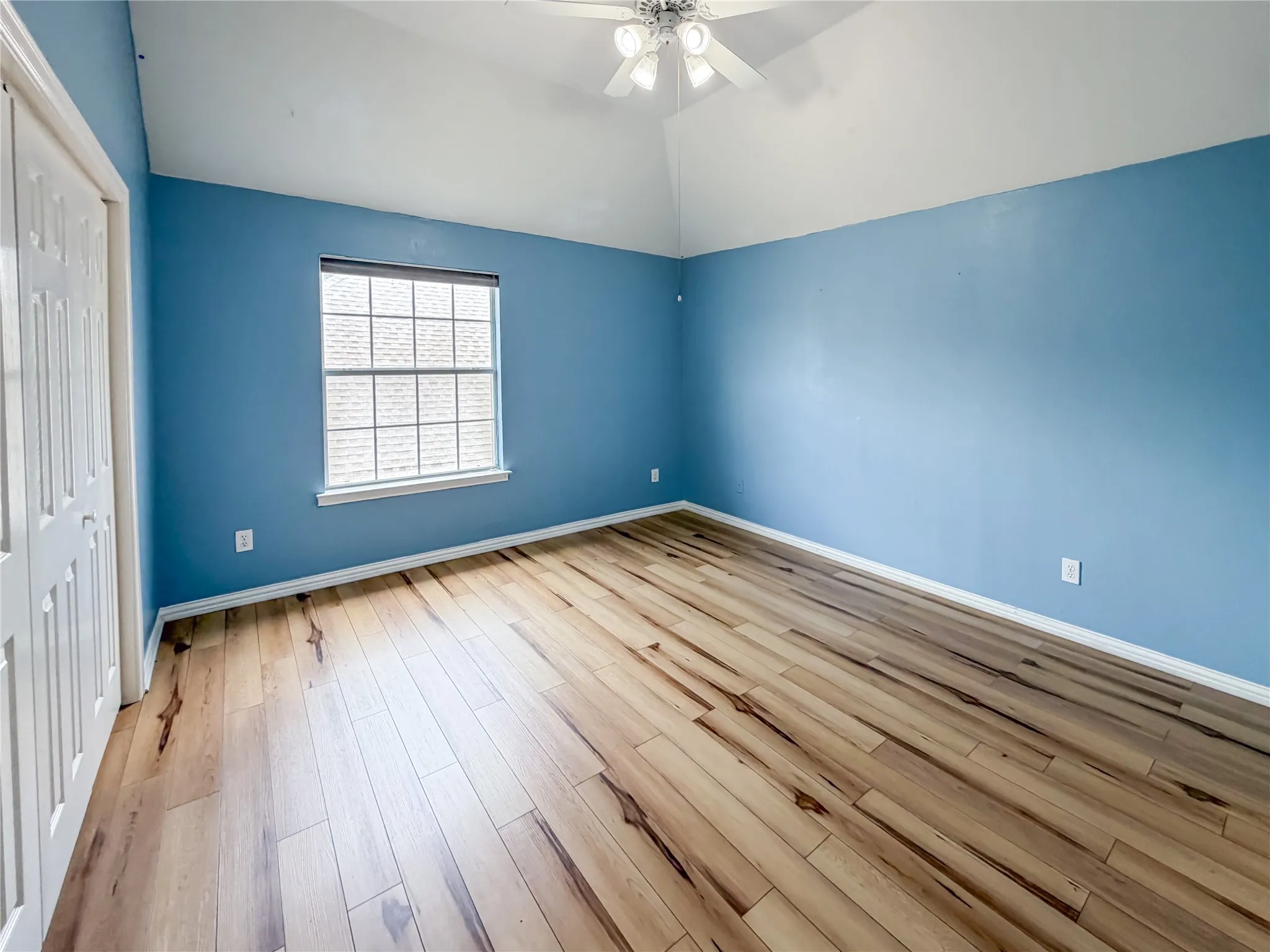Spacious room featuring wood-finish flooring and a vaulted ceiling
