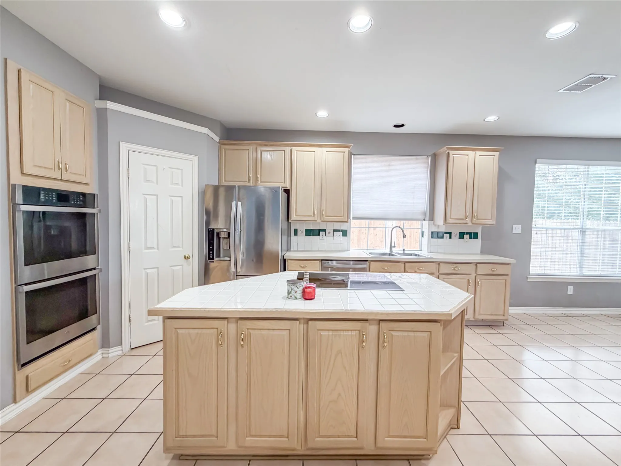 Kitchen featuring a central island with a tiled countertop, wood-finish cabinetry, stainless steel double ovens, and recessed lighting