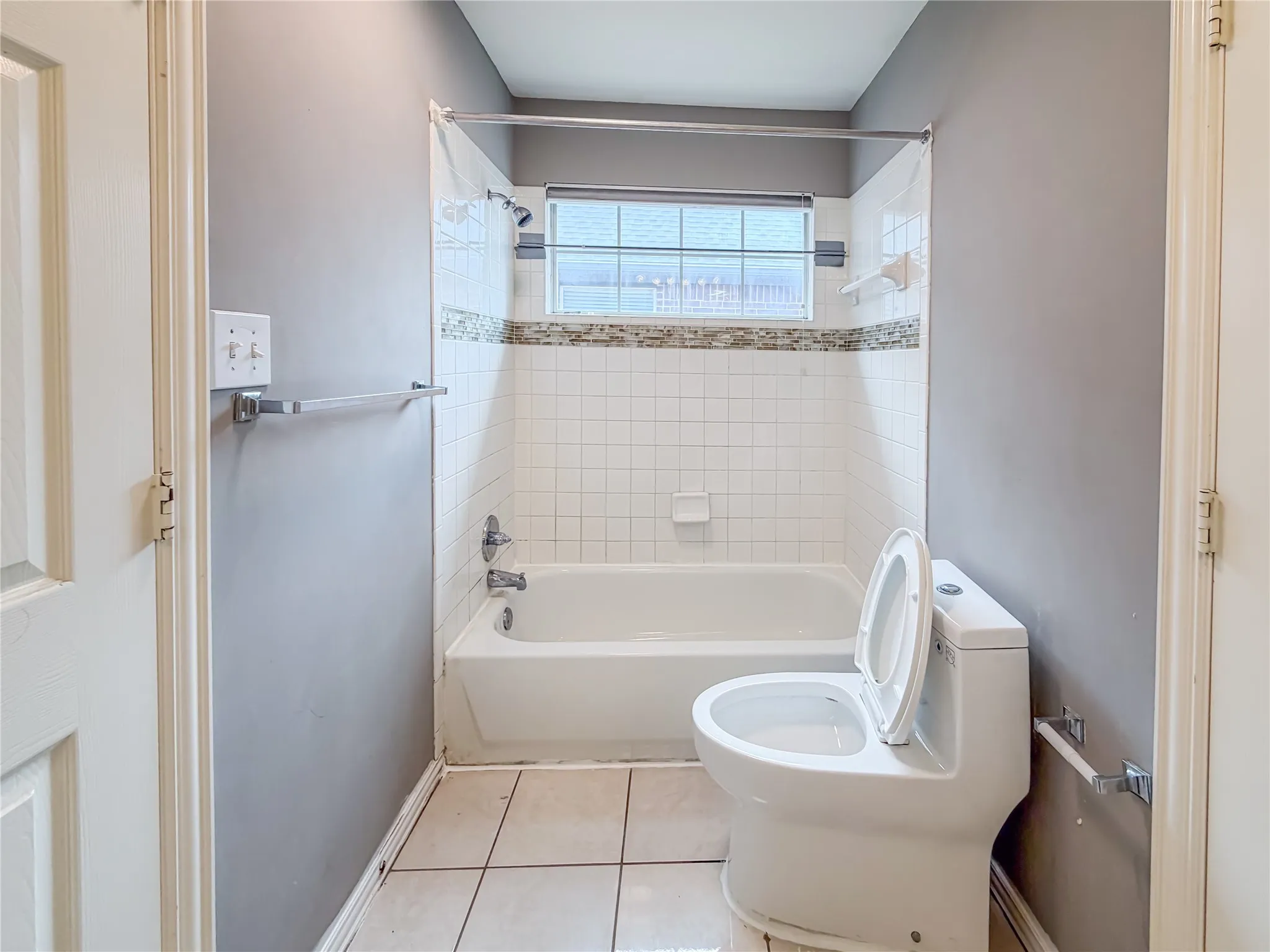 Bathroom featuring a white bathtub, ceramic tile surround, decorative mosaic accent tile, and a single window with privacy blinds