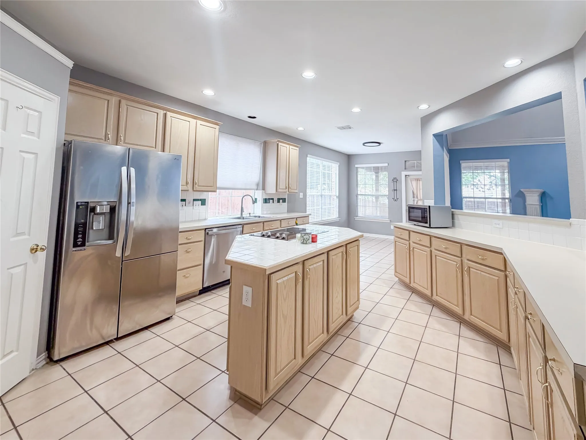 Spacious kitchen featuring a central island with a cooktop, extensive light wood cabinetry, and neutral-toned tile flooring