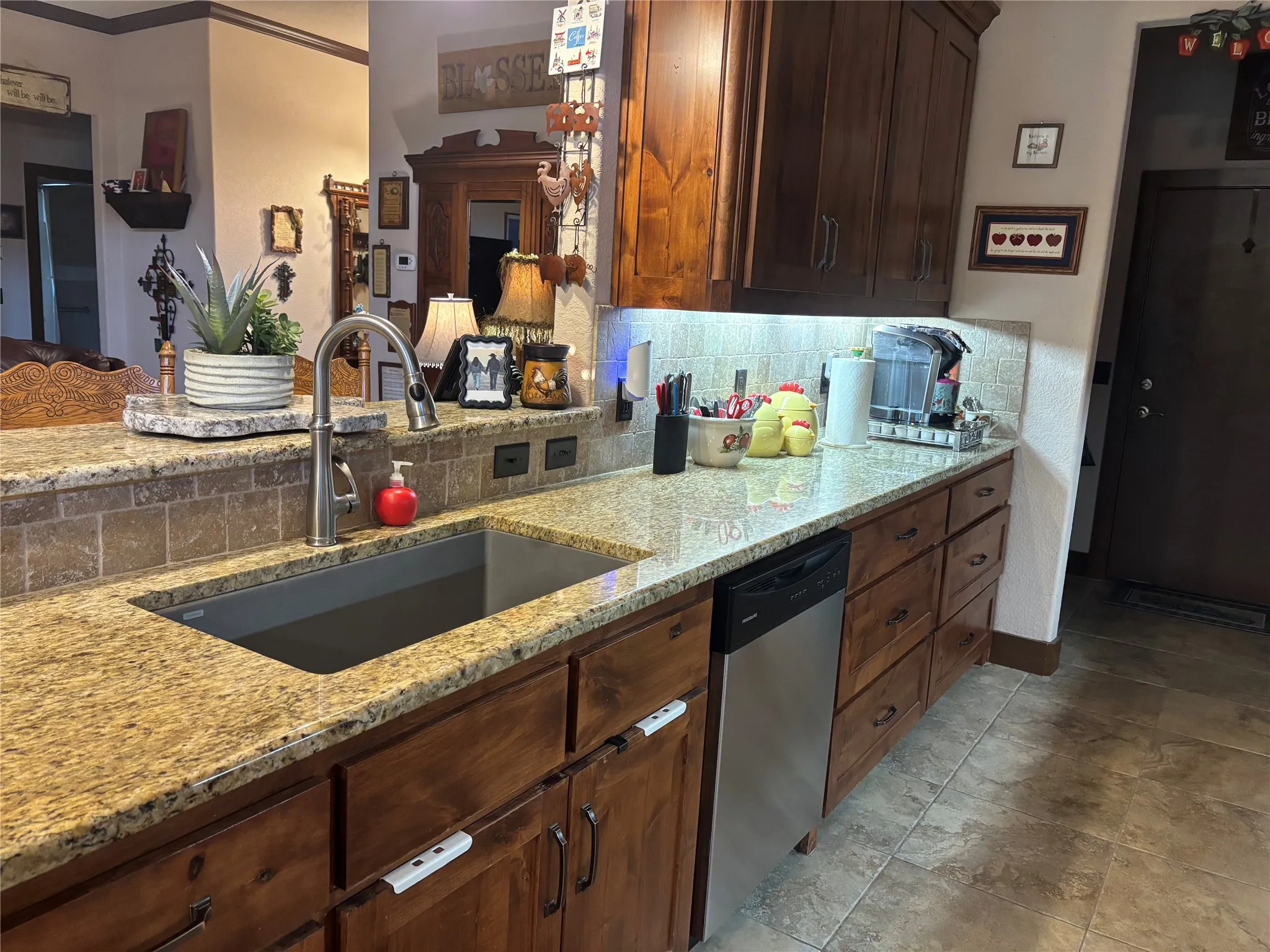 Kitchen featuring granite countertops, a stainless-steel sink with a gooseneck faucet, full-height tile backsplash, and wood cabinetry