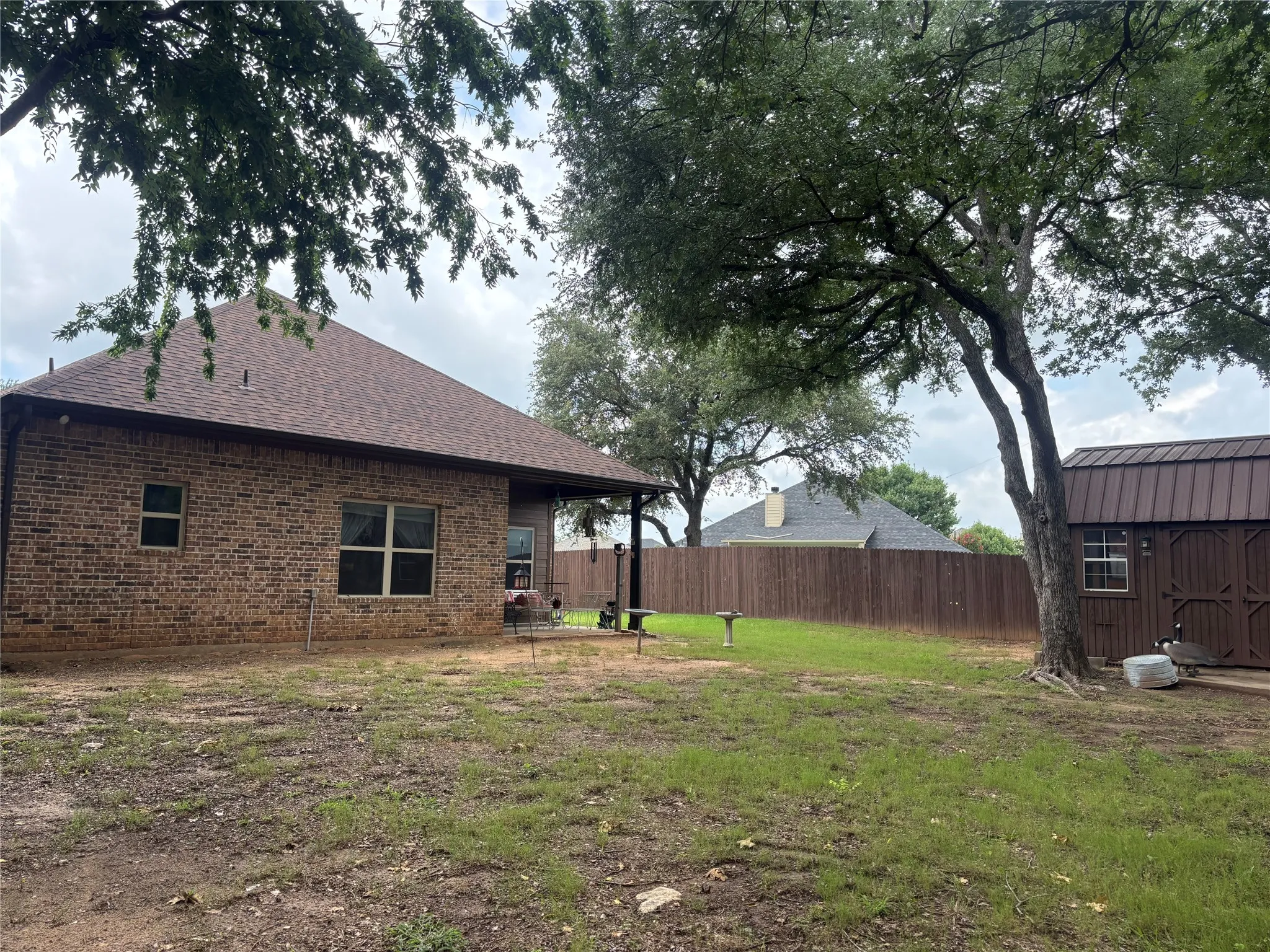Spacious backyard featuring a brick exterior, covered patio, wood fencing, and a detached storage shed