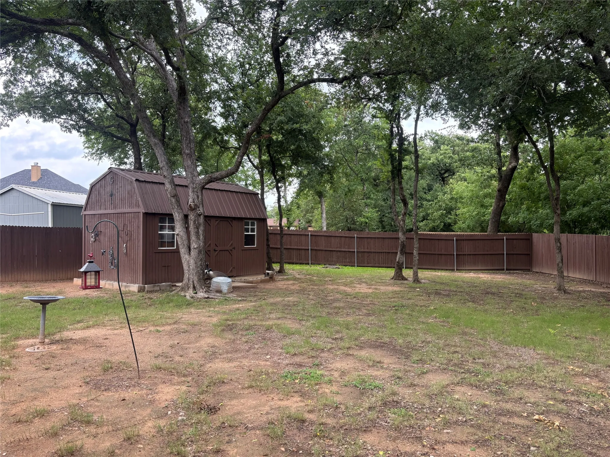 Expansive backyard featuring a brown storage shed with a gambrel roof, white-framed windows, and a wood-paneled exterior