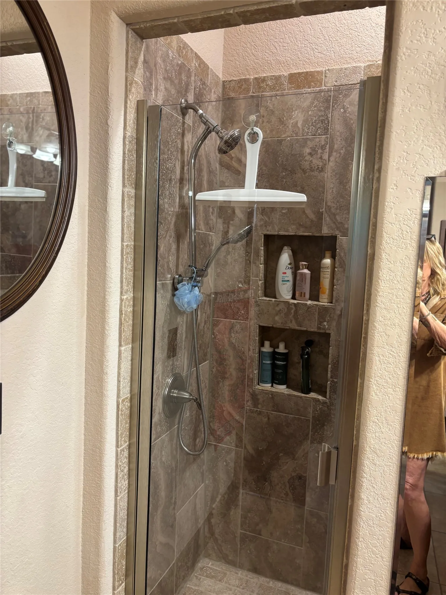 Tiled walk-in shower featuring a glass enclosure with brushed nickel hardware, dual shower heads, and integrated shelving niches