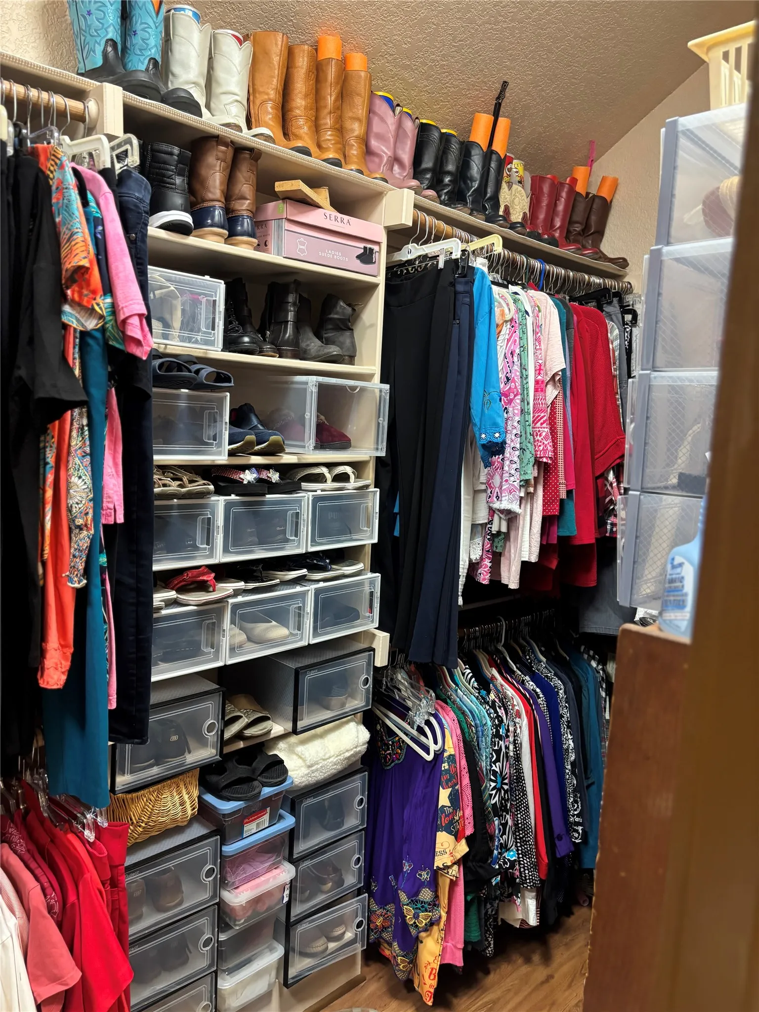Custom closet system featuring built-in shelving, multiple hanging rods, and wood-finish flooring