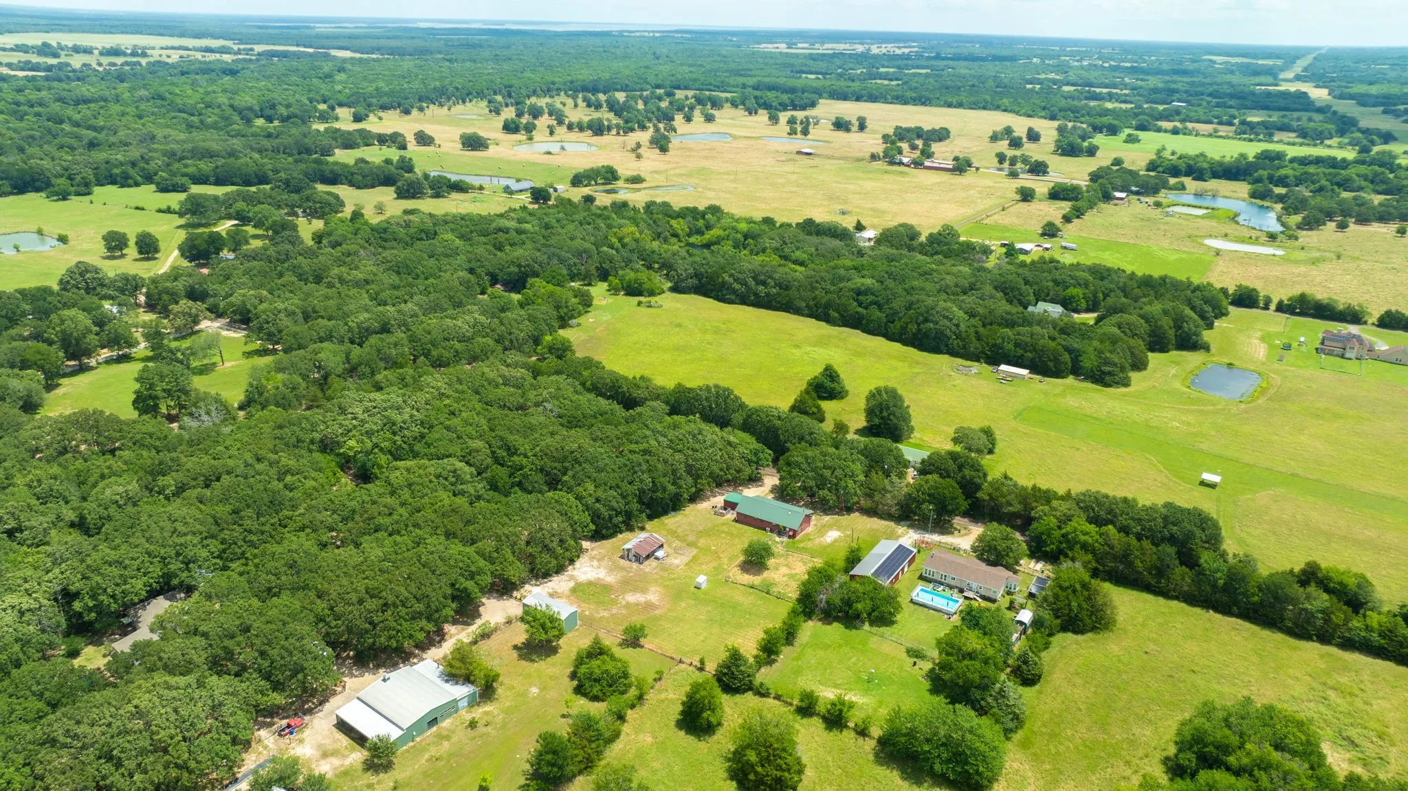 Expansive property featuring a main residence, multiple auxiliary structures, wooded areas, open pastures, and a private swimming pool