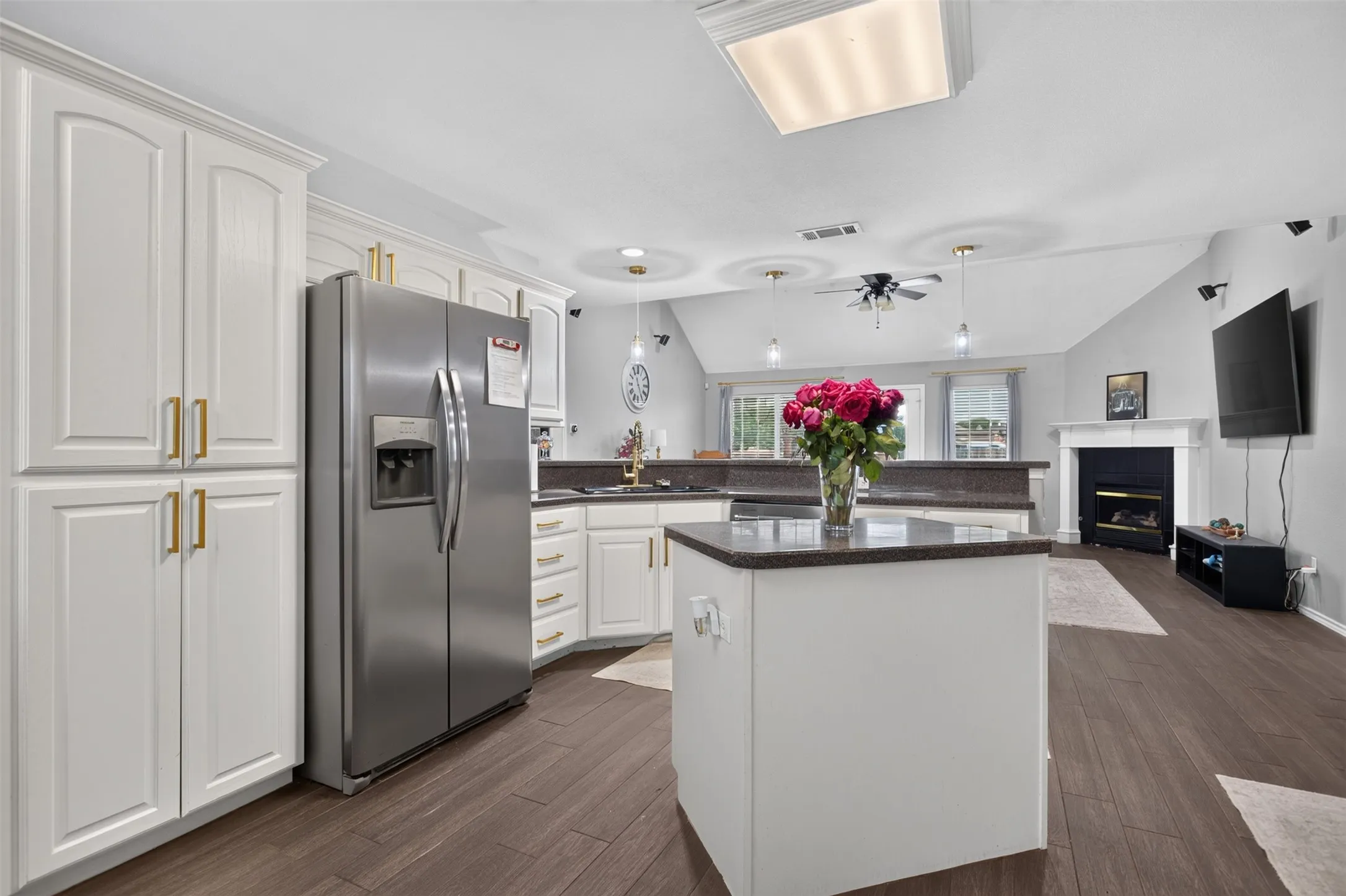 Kitchen with white cabinetry, stainless steel refrigerator, dark countertops, and wood-finish flooring