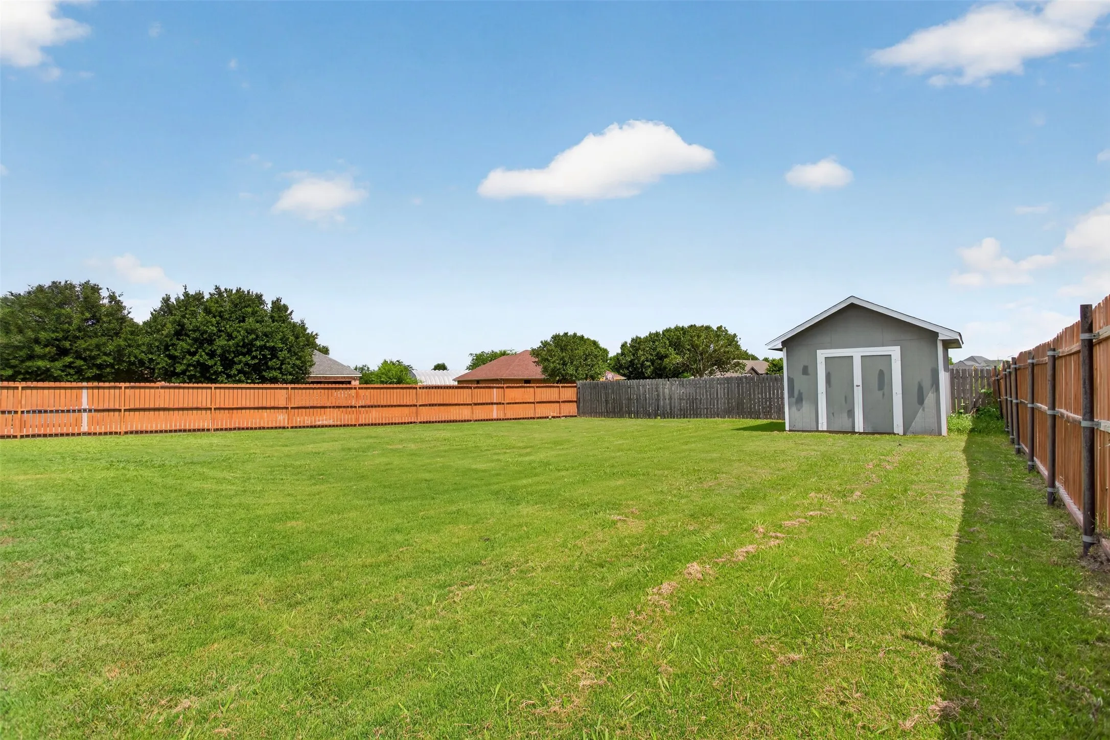 Expansive green lawn featuring a privacy fence, a detached storage shed, and mature perimeter trees