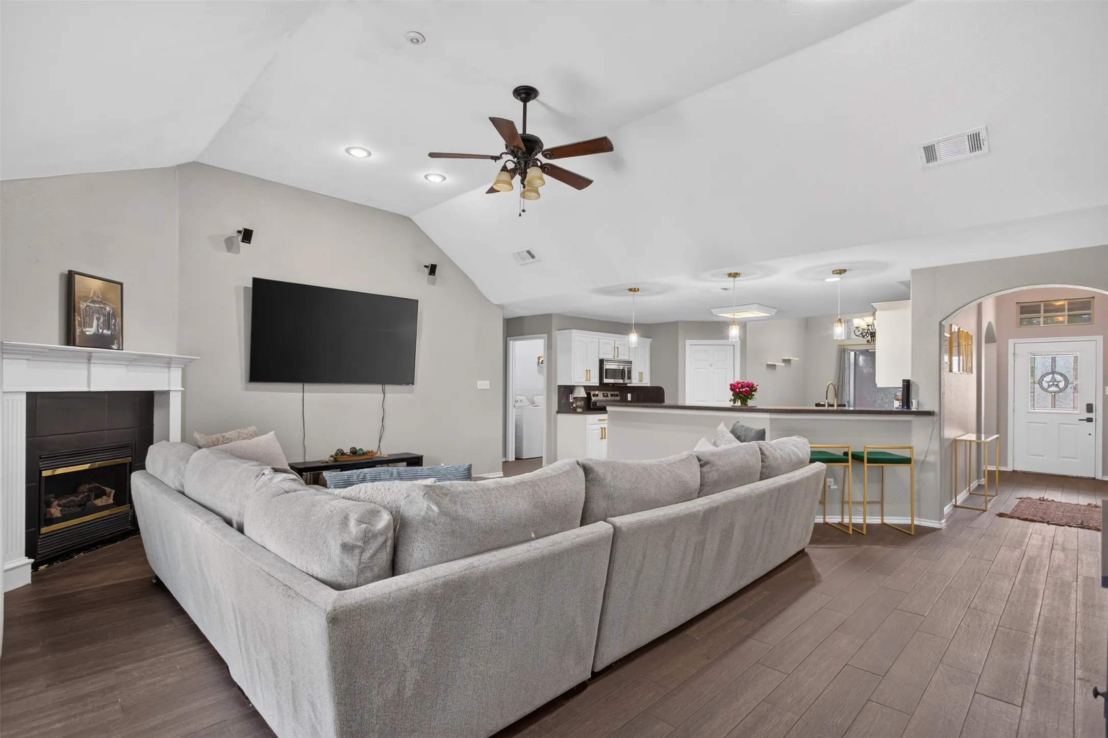 Spacious living area featuring wood-finish flooring, a white mantel fireplace, and a vaulted ceiling with a ceiling fan