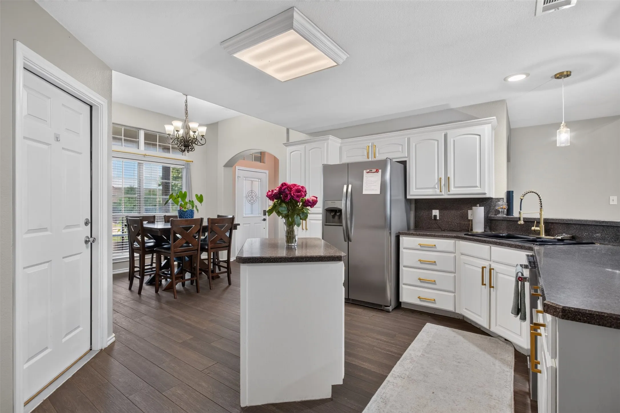 Kitchen featuring white cabinetry with gold-toned hardware, dark countertops, and wood-finish flooring