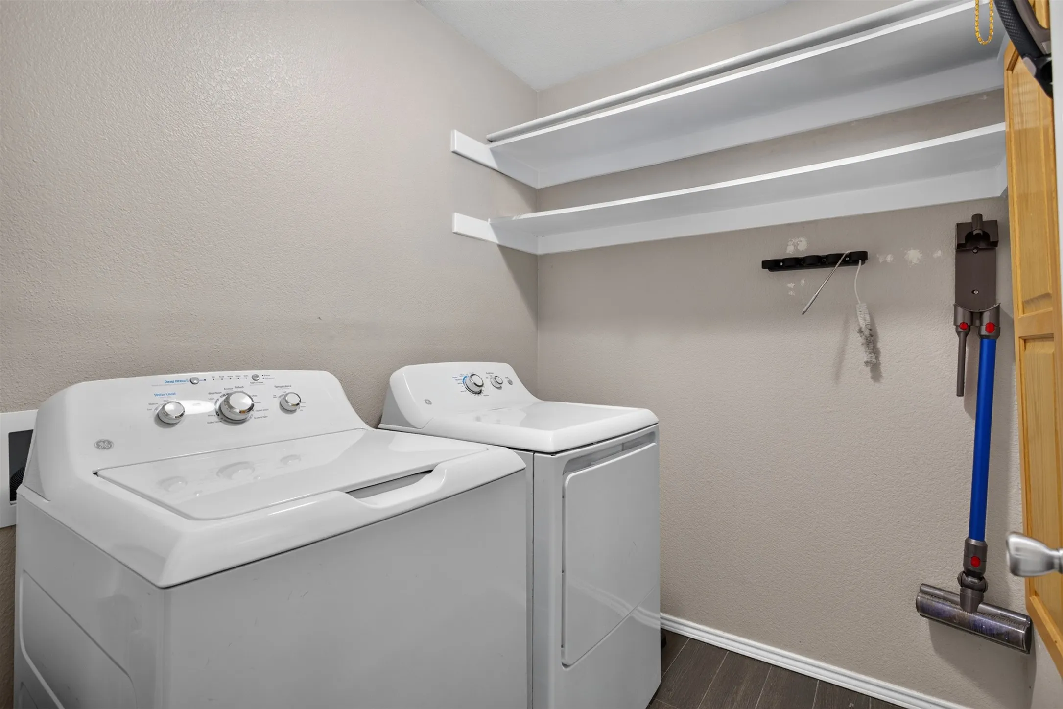 Dedicated laundry space featuring neutral wall paint, two white appliances, wood-finish flooring, and two integrated wall shelves