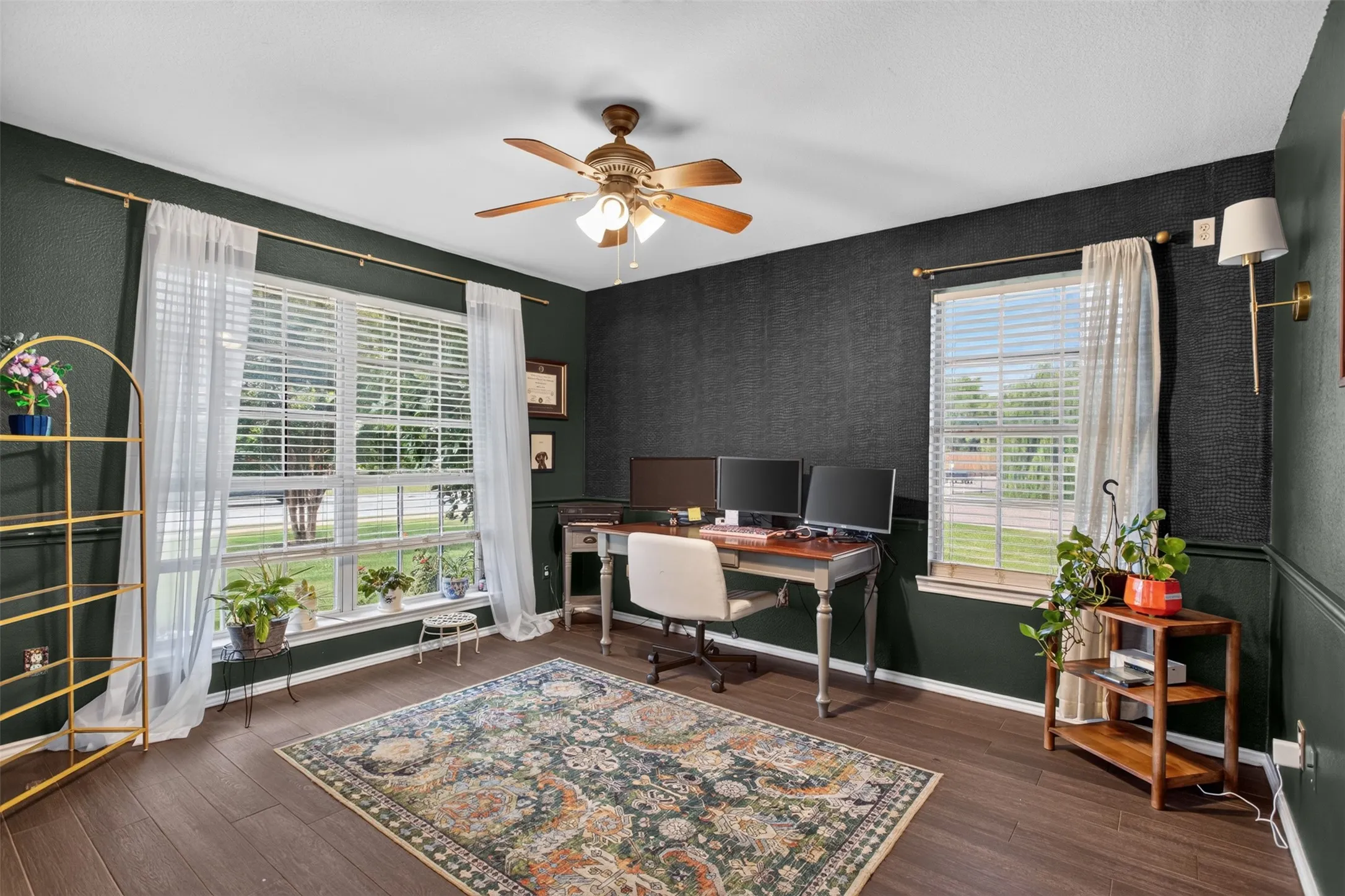 Spacious room featuring dark-toned walls with wainscoting, wood-finish flooring, and a ceiling fan with integrated lighting
