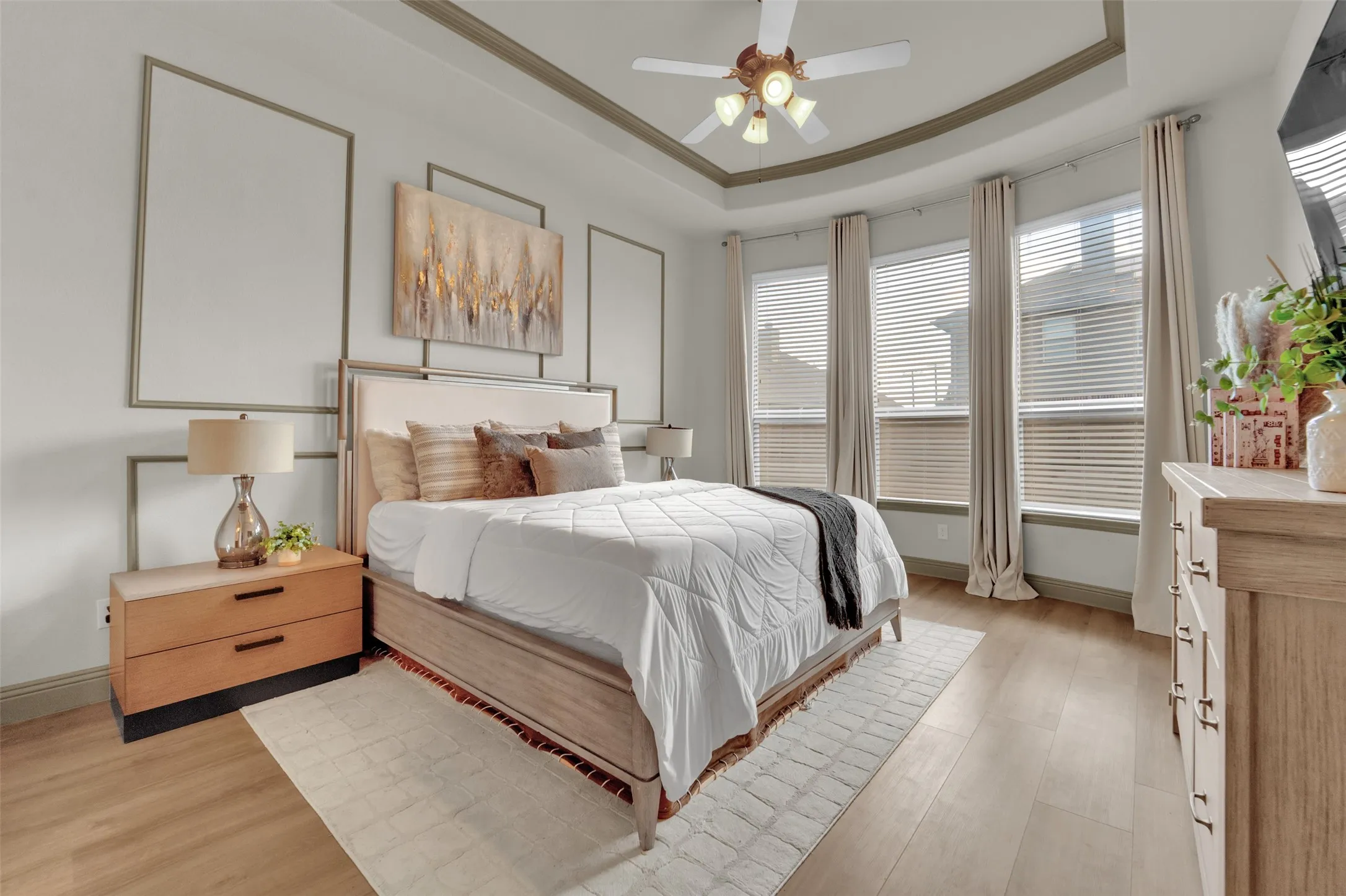 Bedroom featuring wood-finish flooring, bay windows, tray ceiling, and decorative wall molding