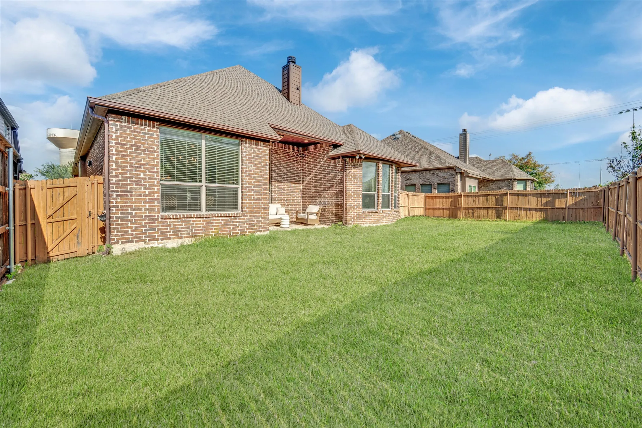 Spacious backyard featuring a manicured lawn, full privacy fencing, brick exterior, bay window, and a gabled roofline
