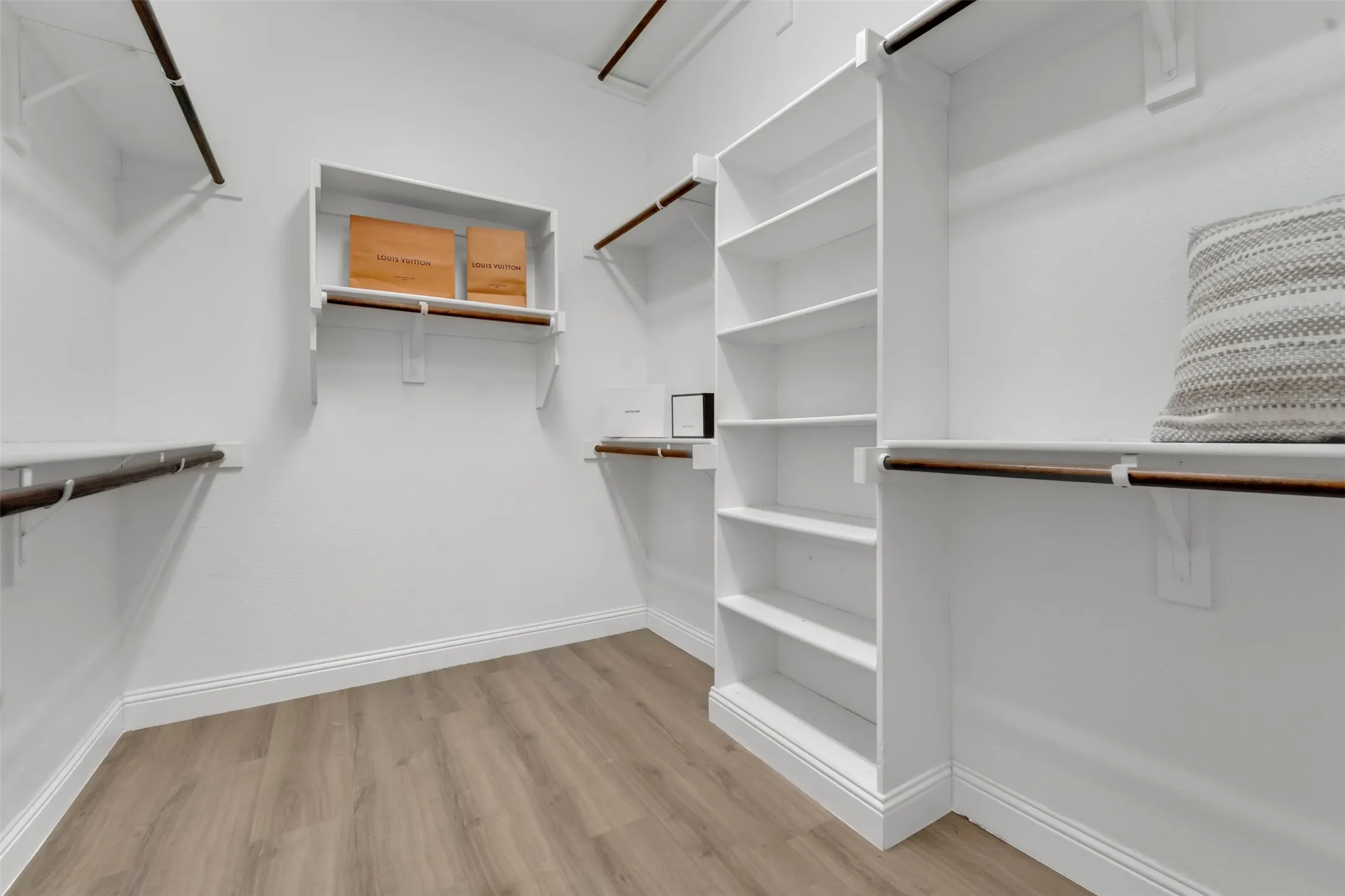 Spacious walk-in closet featuring wood-finish flooring, white baseboards, multiple hanging rods, built-in shelving, and recessed lighting