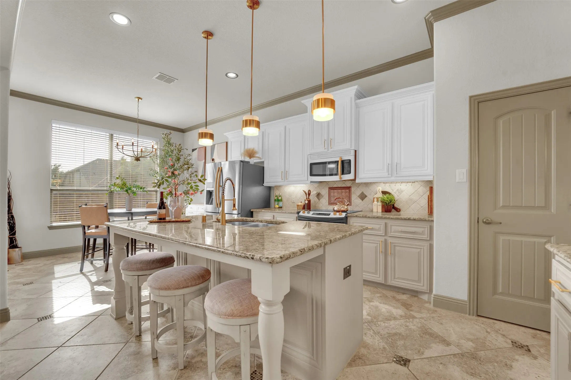 Open-concept kitchen featuring an island with granite countertops, pendant lighting, stainless steel appliances, white upper cabinetry, and light-toned lower cabinetry with a tiled backsplash