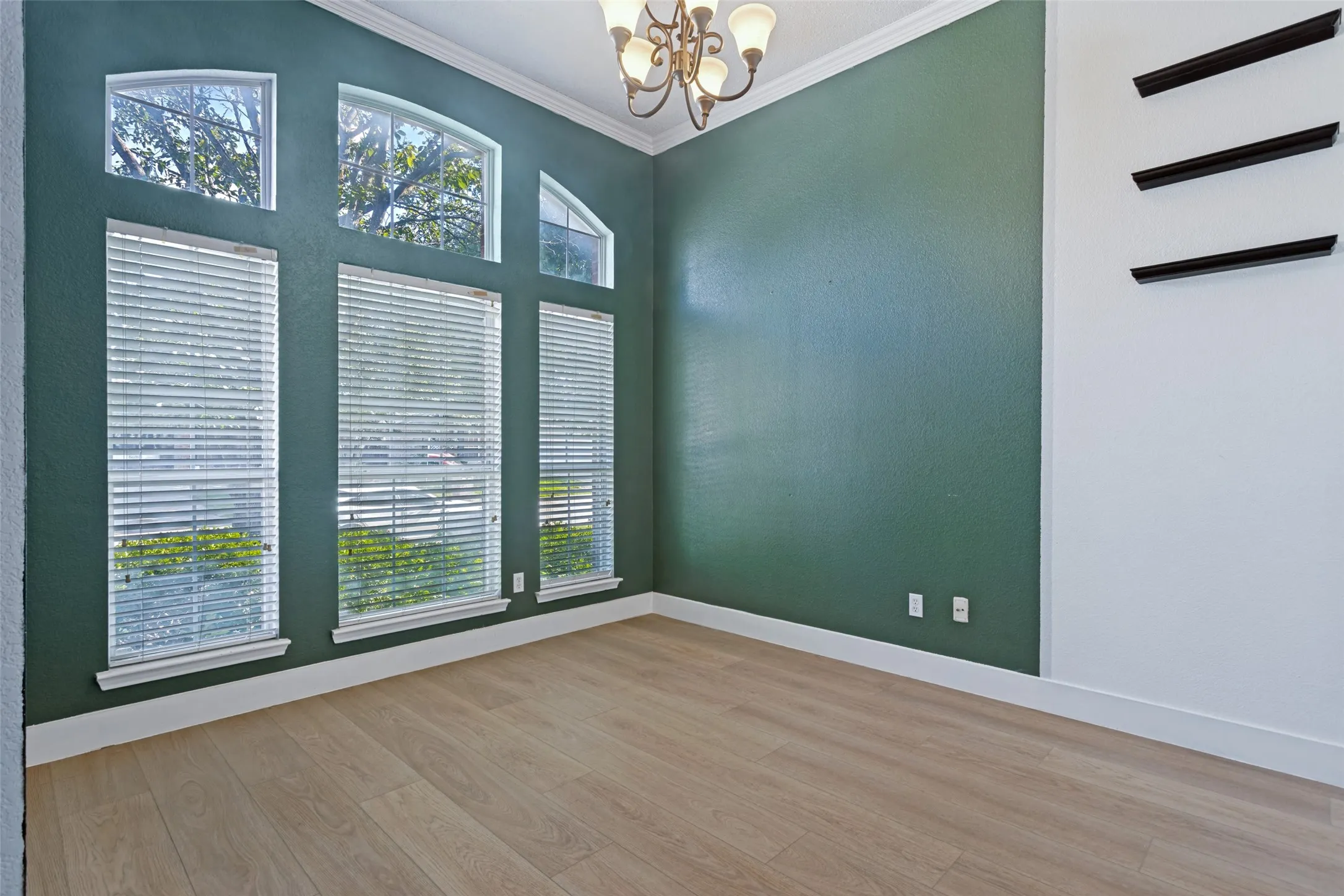 Room featuring a high ceiling with crown molding, a chandelier, and wood-finish flooring