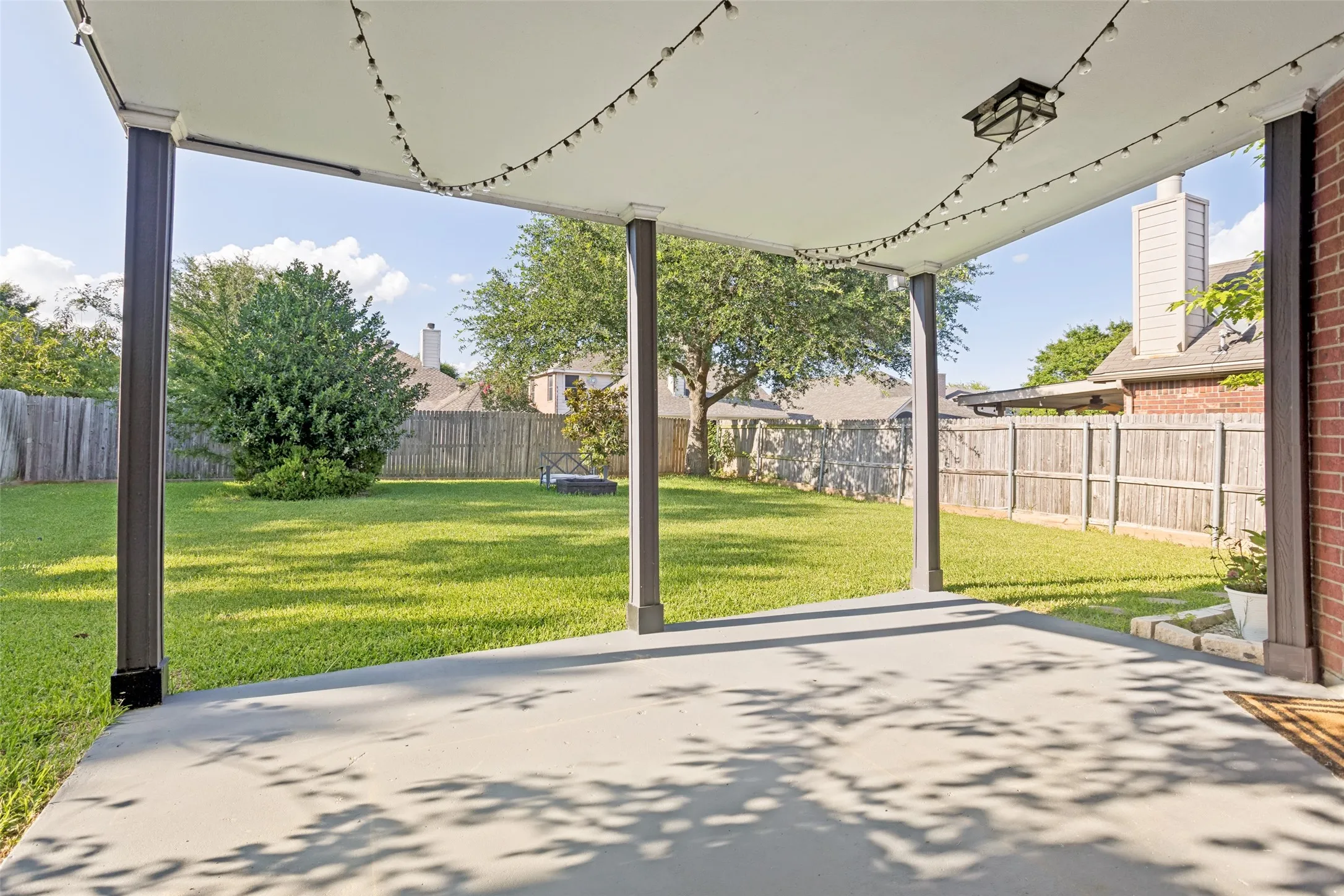 Covered concrete patio with four support columns, an outdoor ceiling light fixture, and string lights