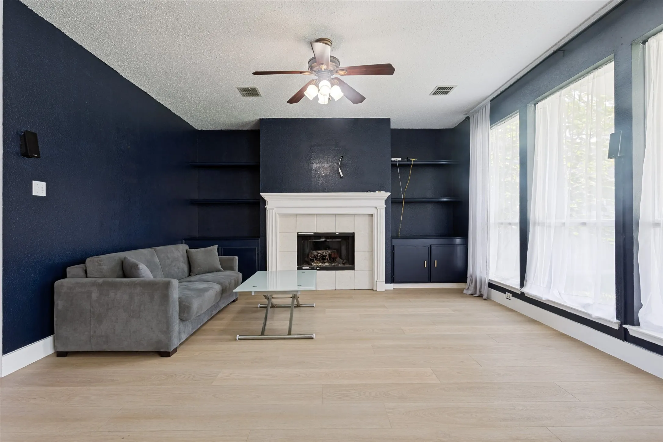 Spacious living area featuring light wood-finish flooring, a fireplace with a white mantel, and built-in shelving and cabinetry