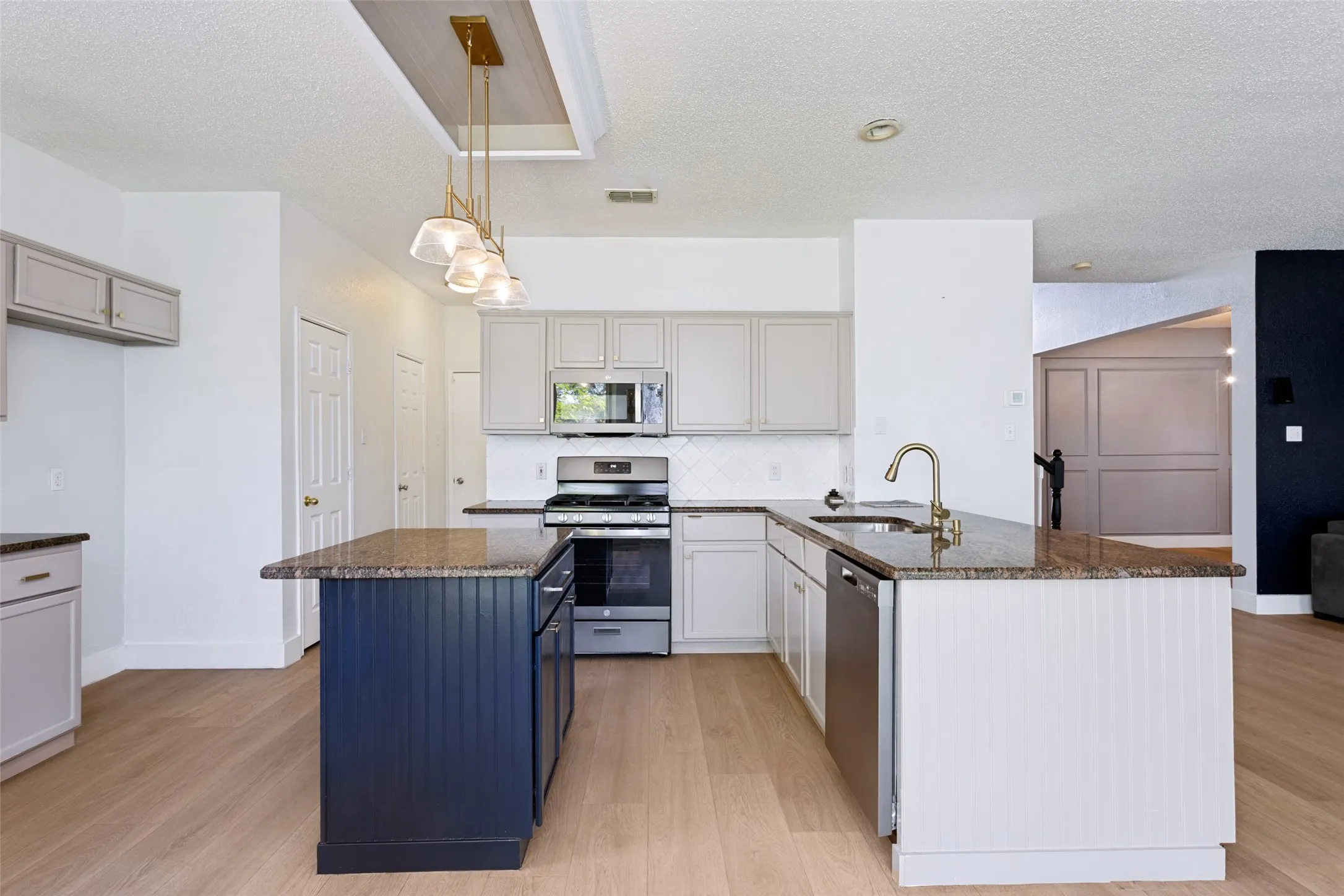 Modern kitchen featuring an island with a blue beadboard base, stone countertops, stainless steel appliances, and wood-finish flooring