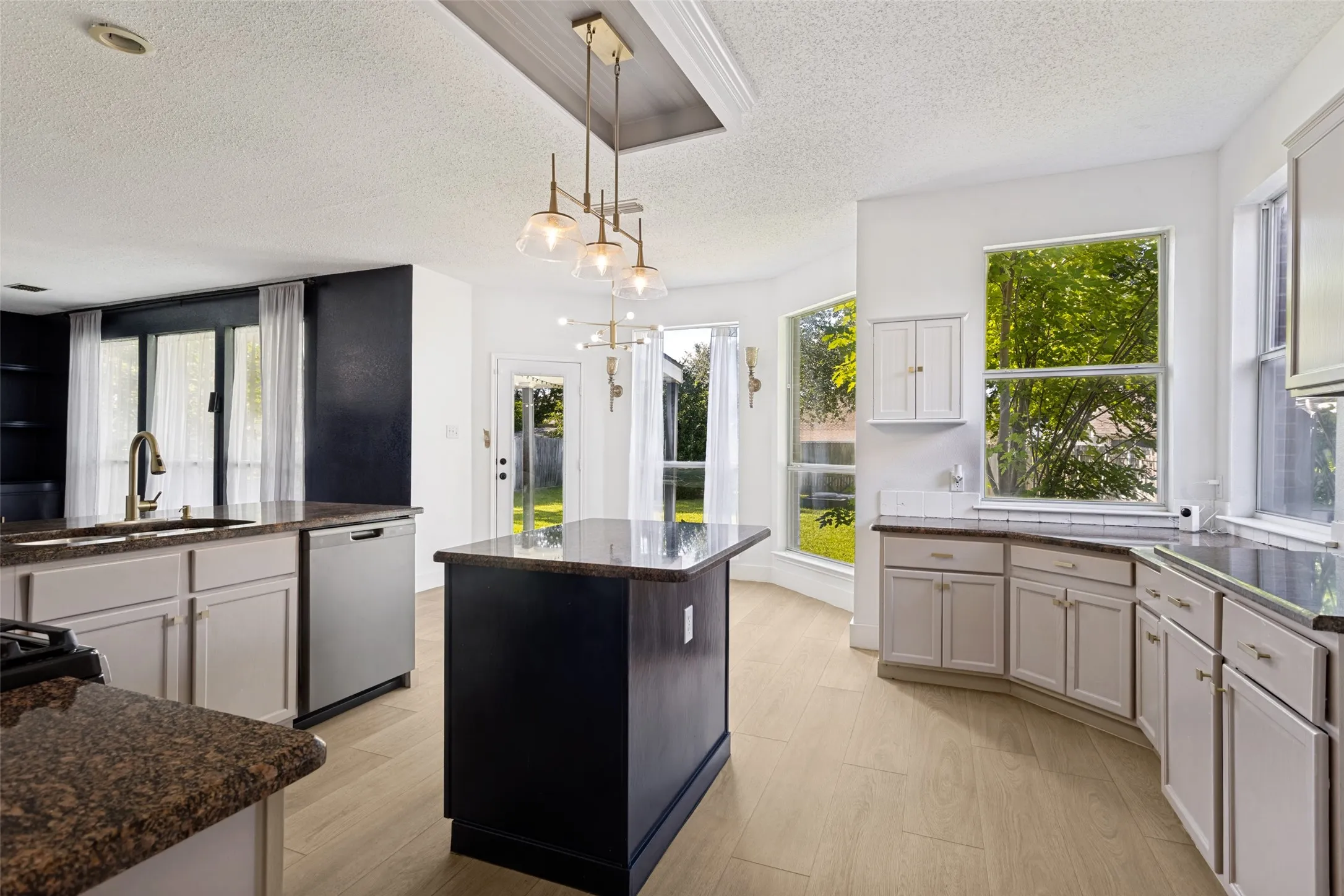Open-concept kitchen featuring an eat-at island, granite countertops, light wood-finish flooring, white cabinetry, and stainless steel appliances