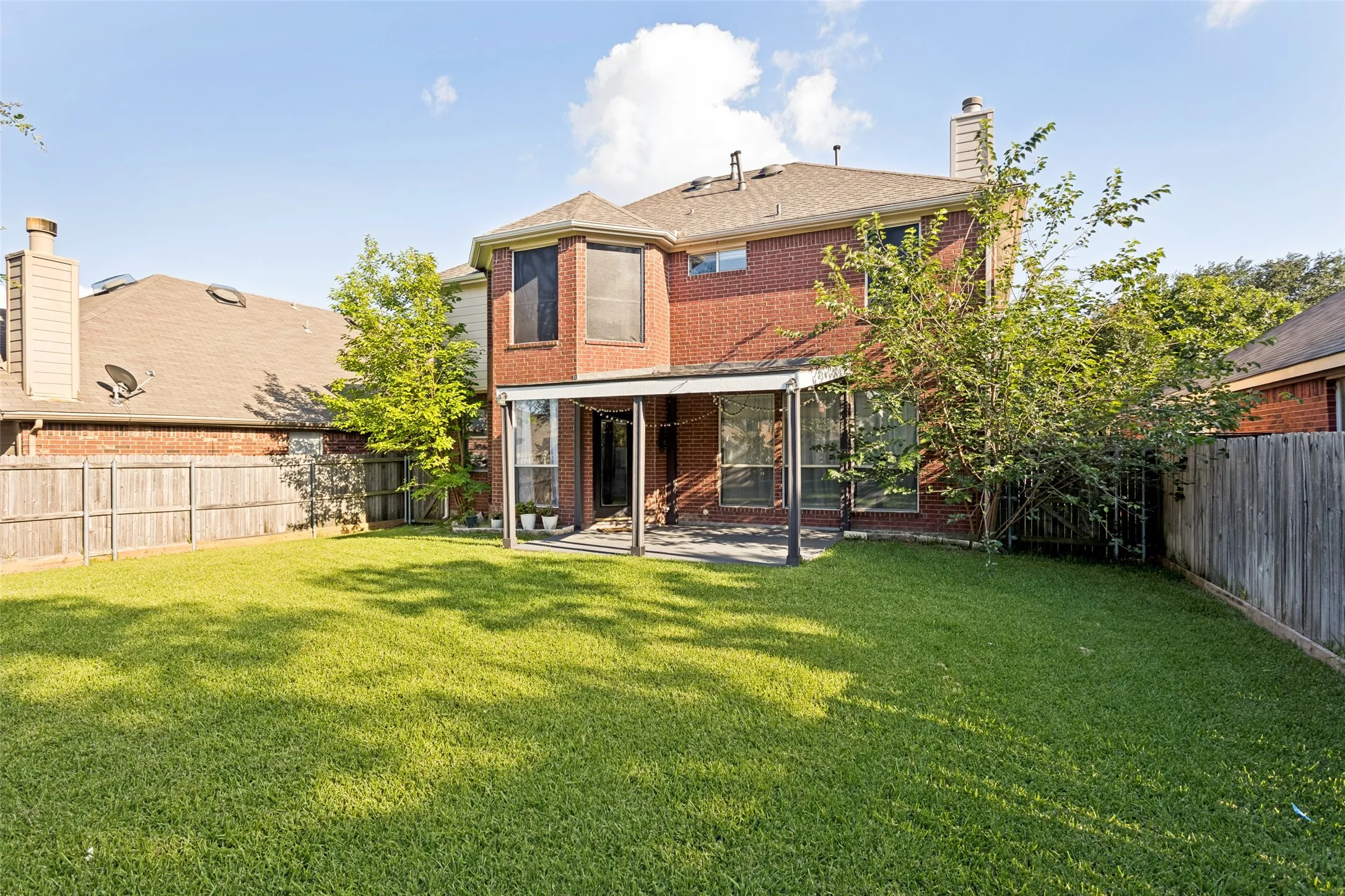 Spacious backyard featuring a covered patio, expansive lawn, mature trees, and a privacy fence