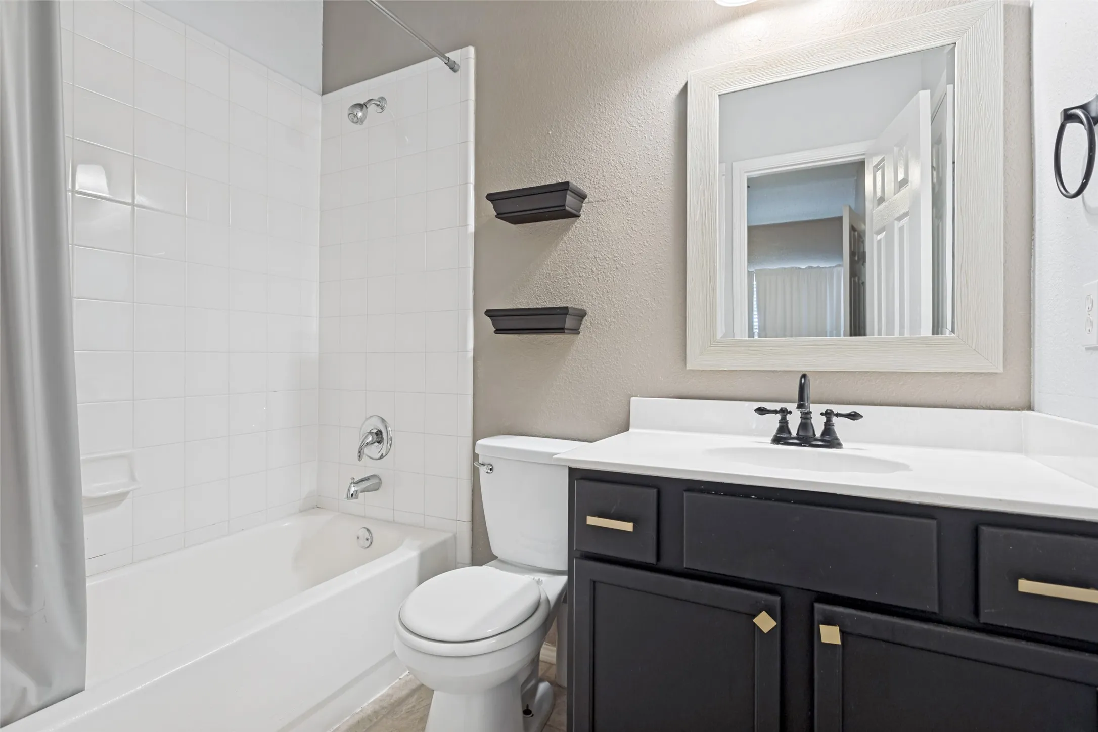Bathroom featuring a white subway tile tub surround, white countertop, dark wood-finish vanity with gold-tone hardware, and a framed mirror